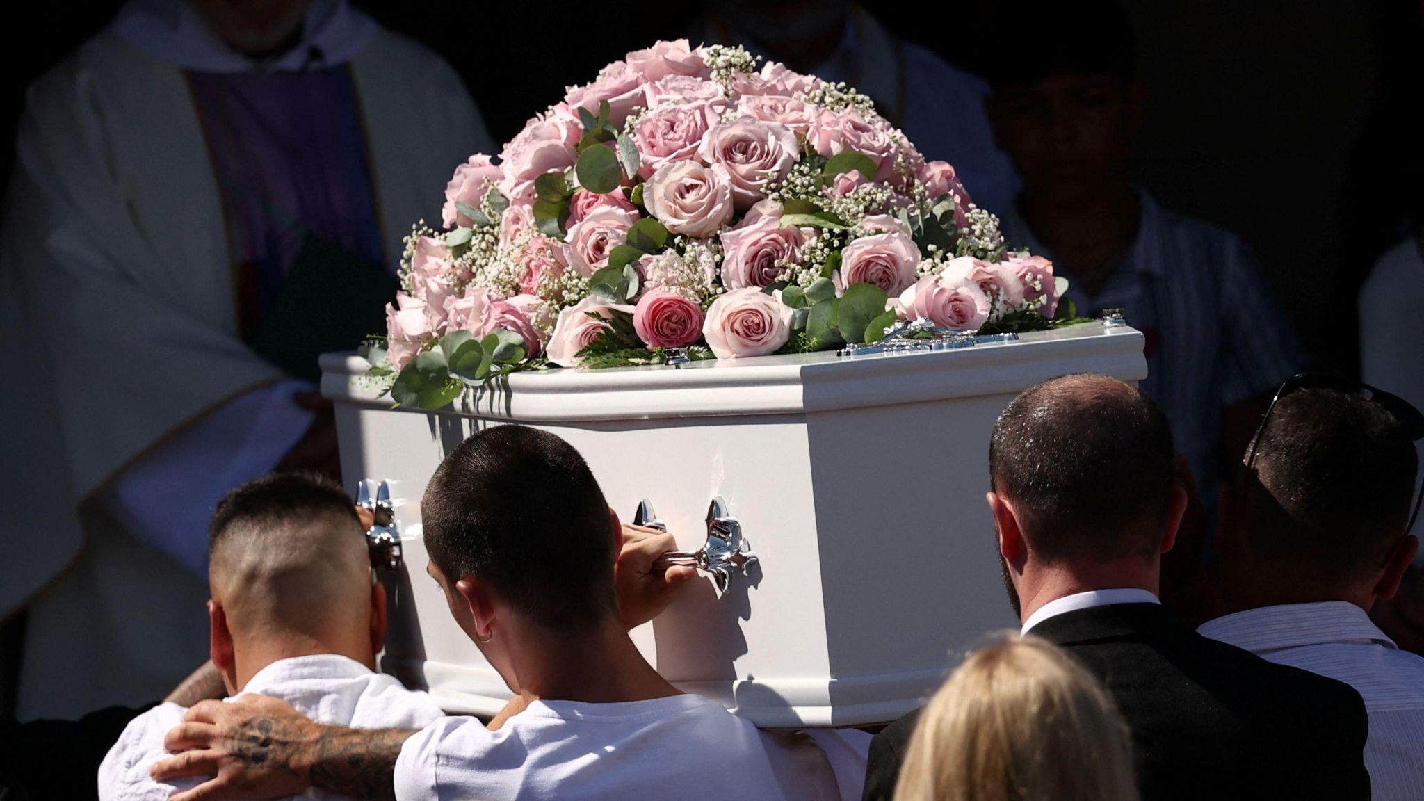 Men carry the coffin of Alice Dasilva Aguiar, topped with pink roses