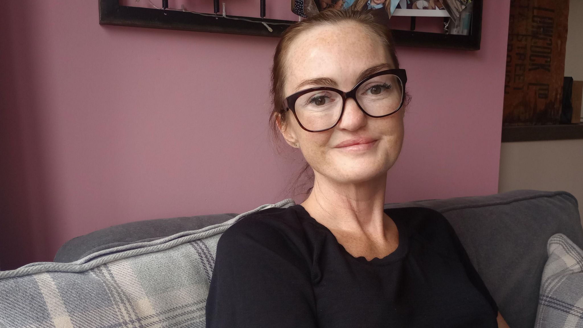 Helen Bone, wearing glasses and with a ponytail, sitting on a checked sofa