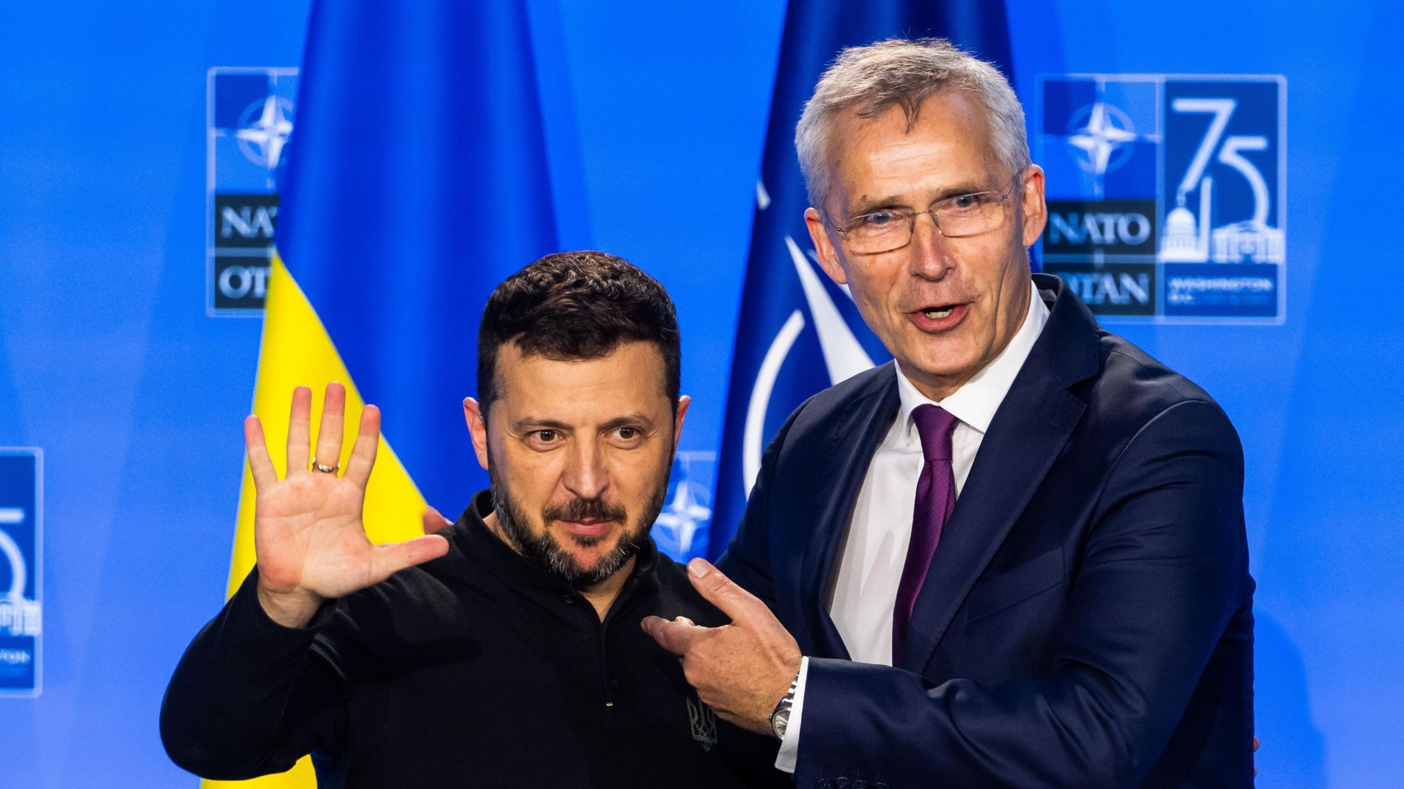 President of Ukraine Volodymyr Zelensky embraces Jens Stoltenberg in front of a Ukrainian flag next to a Nato flag