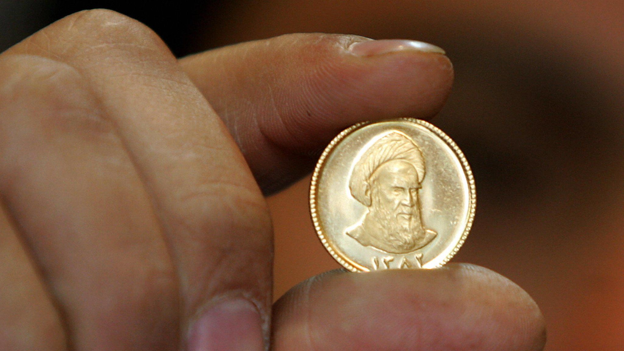 File photo showing an Iranian gold trader holding a gold coin in Tehran (19 April 2006)