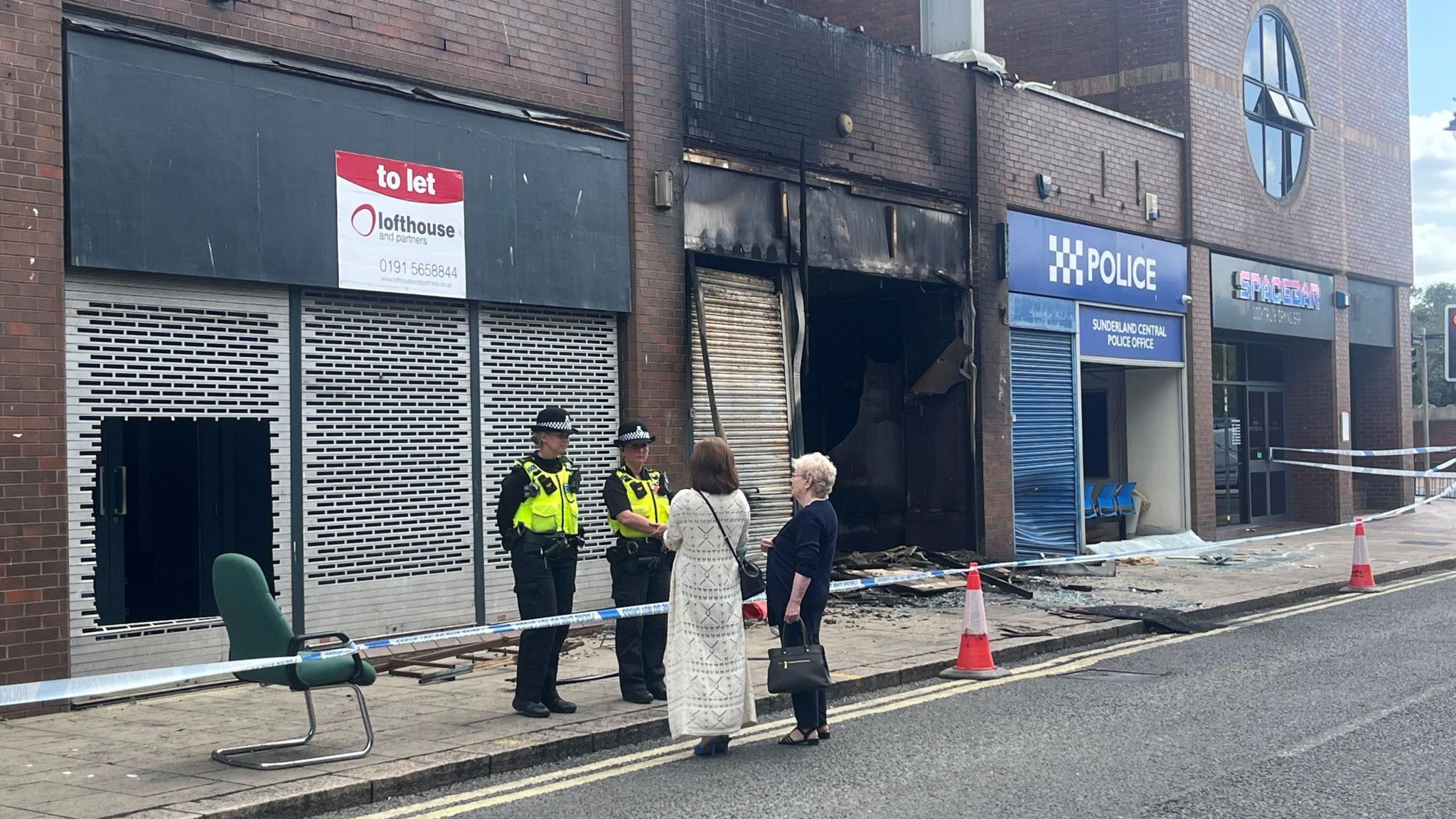 Two police officers stand outside the Citizens Advice officer. They are talking to two women stood on the other side of police tape. The office has been destroyed by the fire.