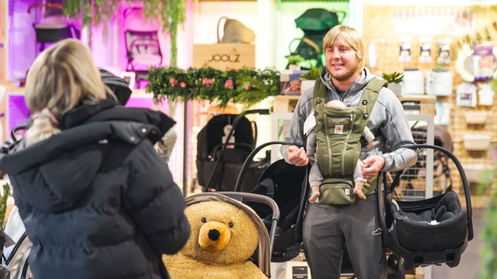 Paddy Pimblett holds two baby carriers and wears a baby sling with a doll whilst his wife Laura looks on.