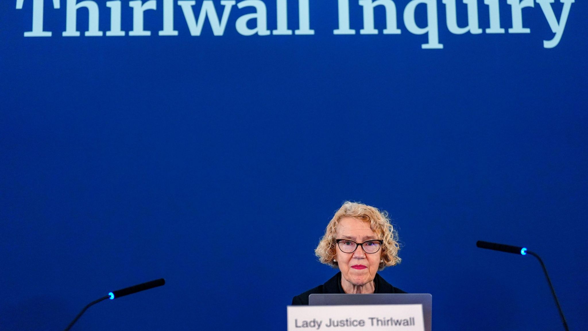 Lady Justice Thirlwall sits ahead of a blue screen with 'Thirlwall Inquiry' projected onto it in large white letters