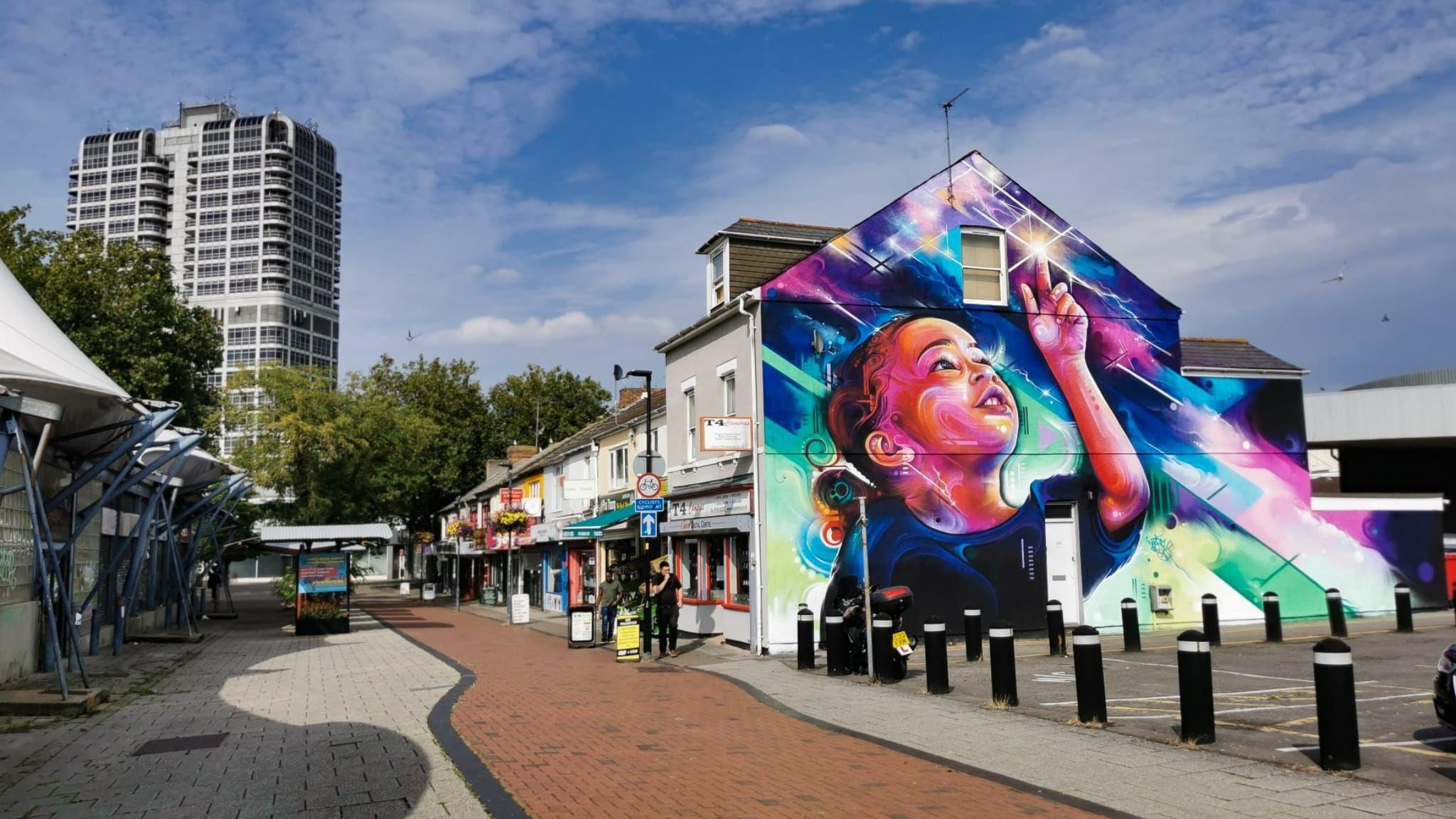 A large mural of a small girl on the side of a building in a town square