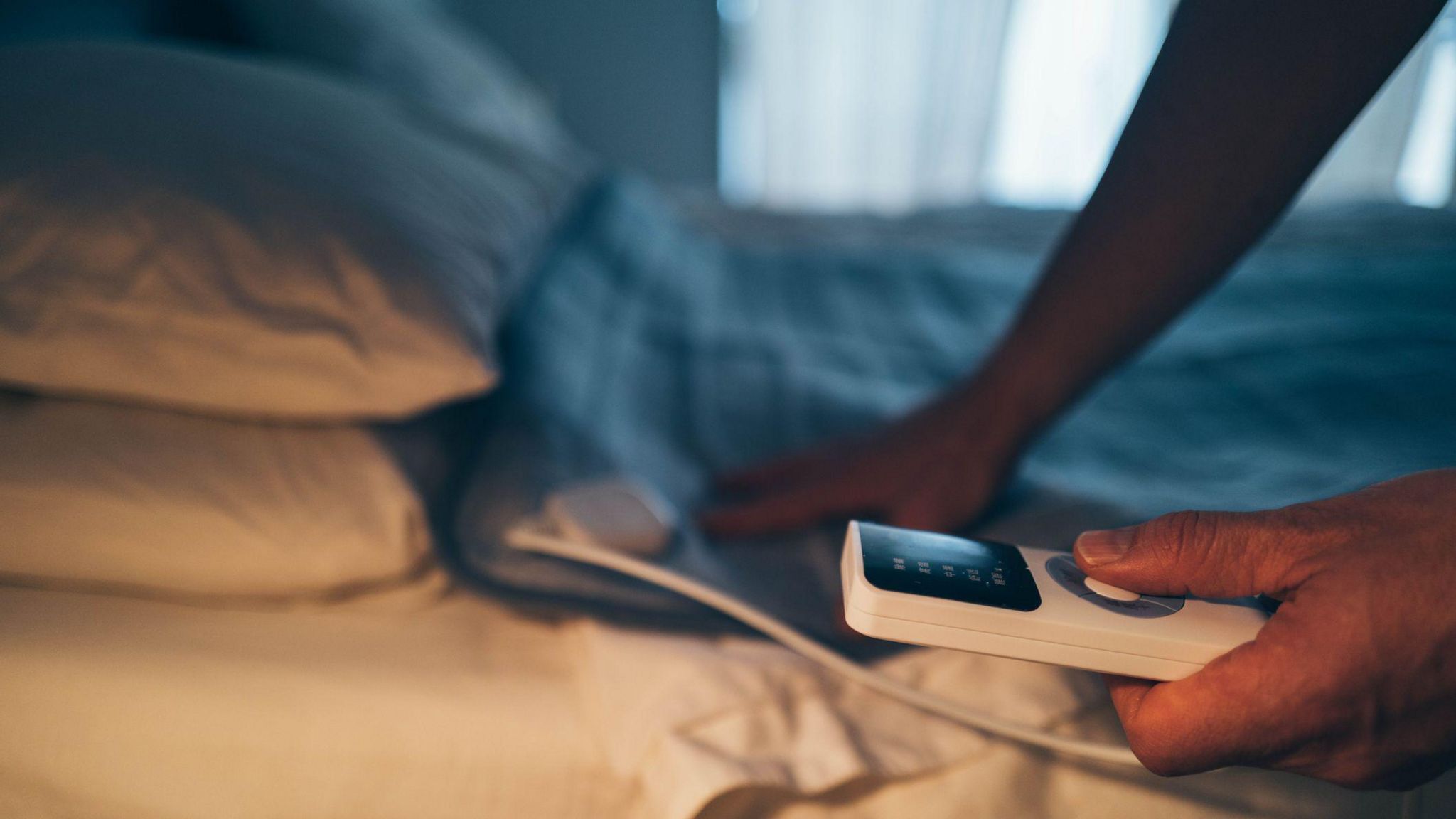 A blue electric blanket on a bed with large white pillows.