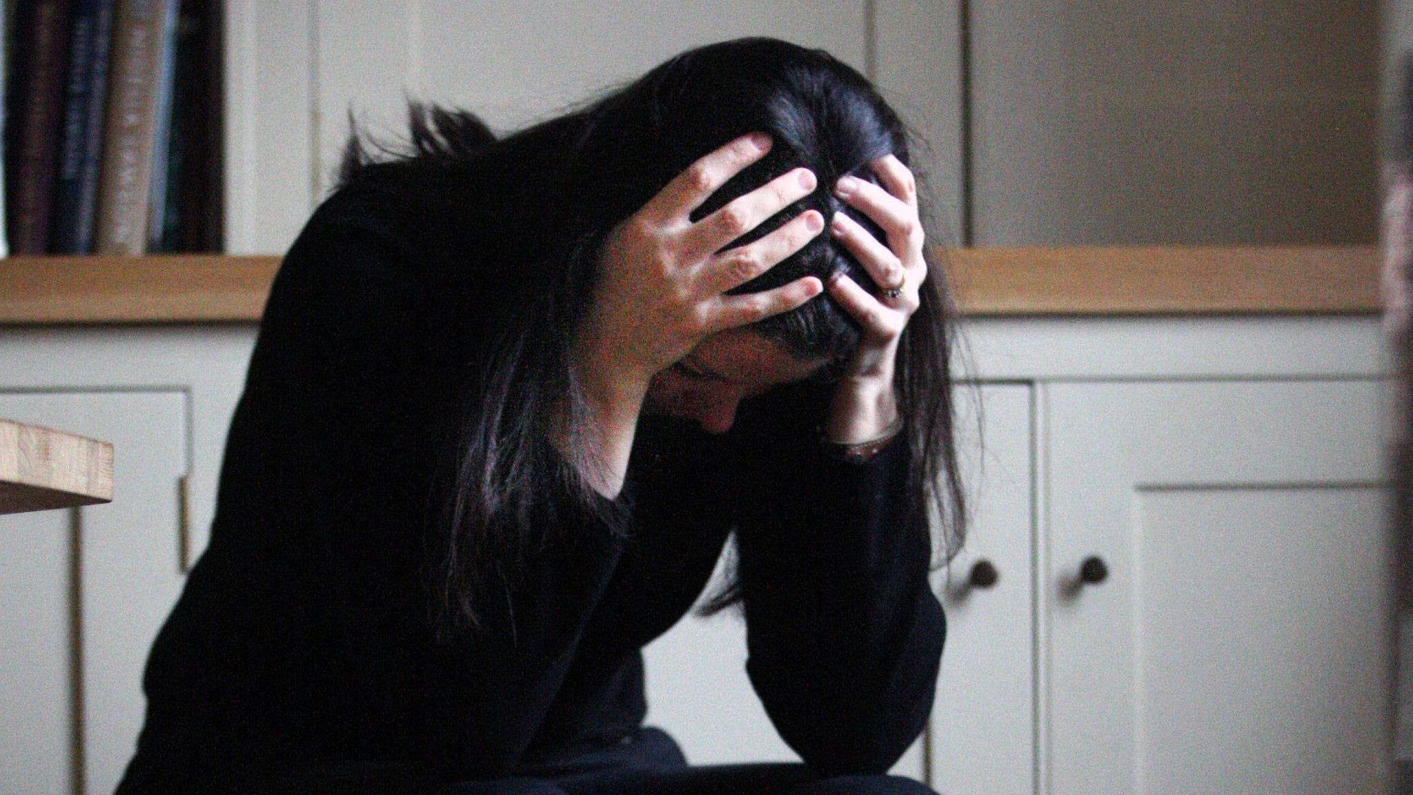 A woman looking distraught, with her hands on her head