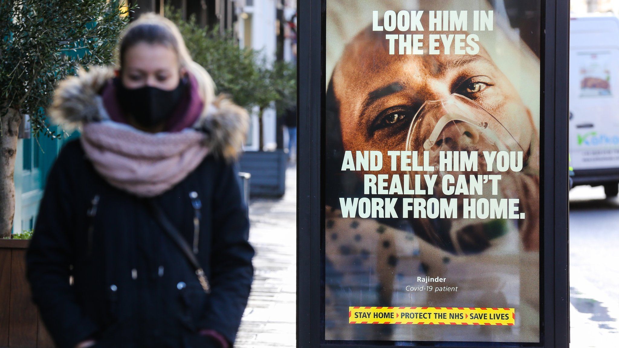 A woman wearing a face mask walks past a Covid-19 NHS campaign poster