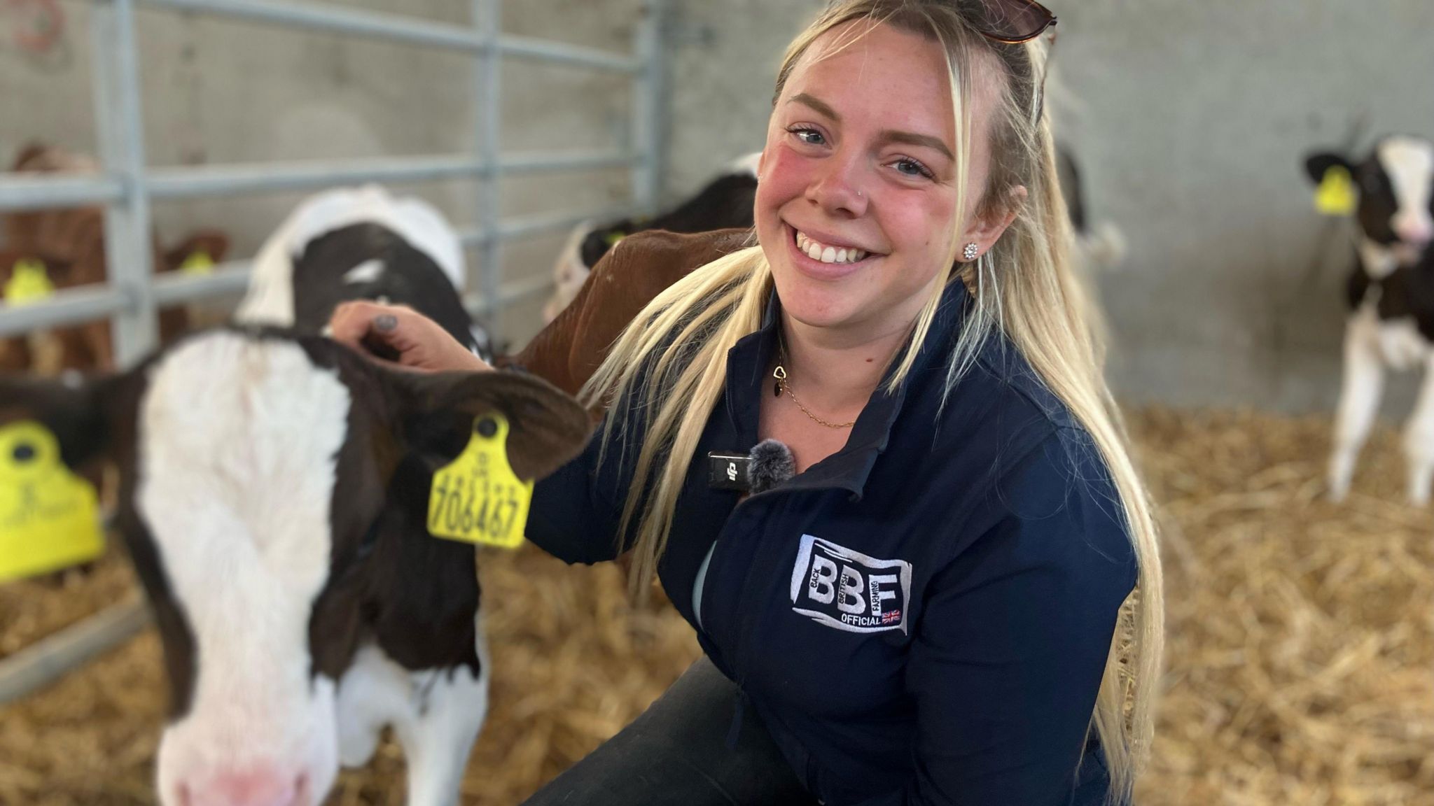 A young blonde woman smiling at the camera and stroking a brown and white calf