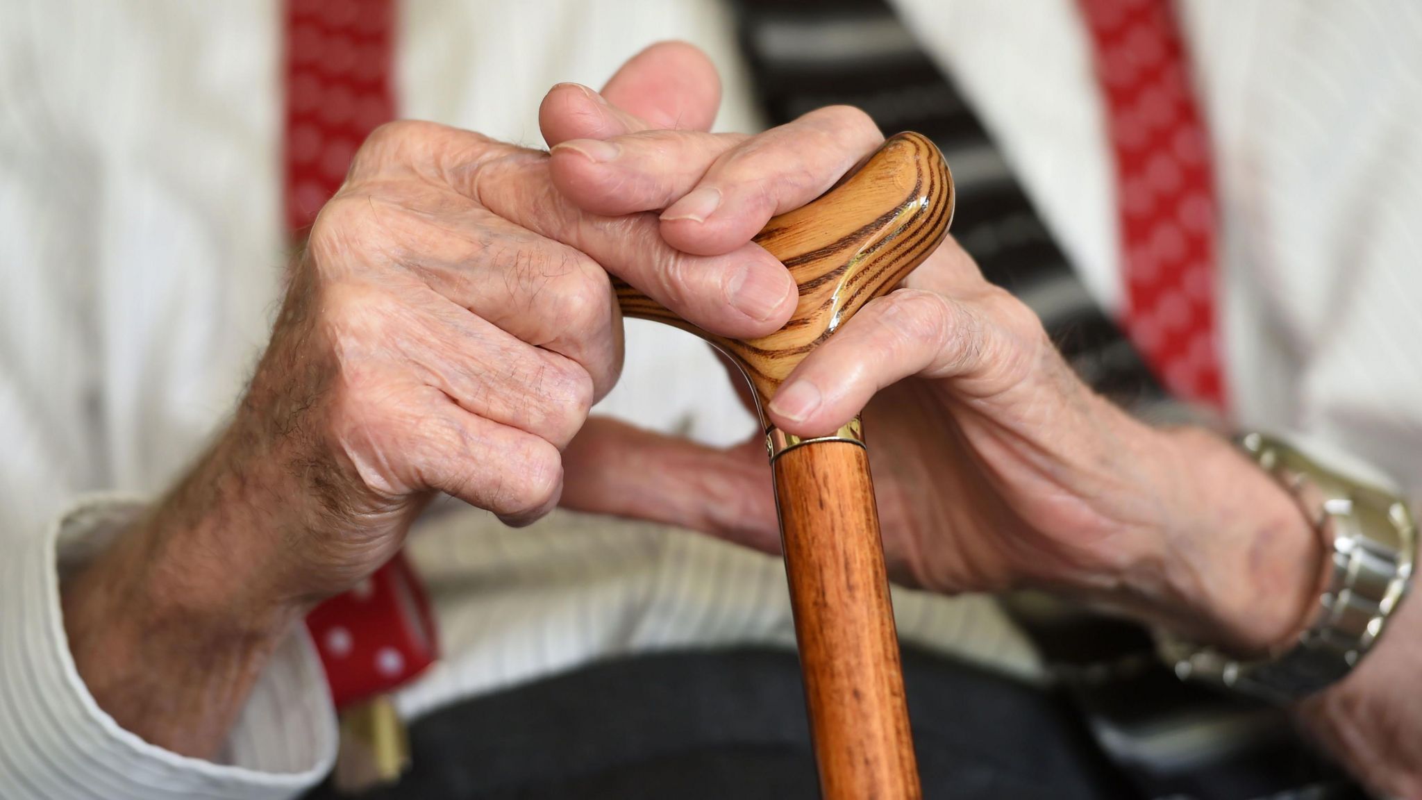 A closeup photo of an elderly man's hands holding a walking stick