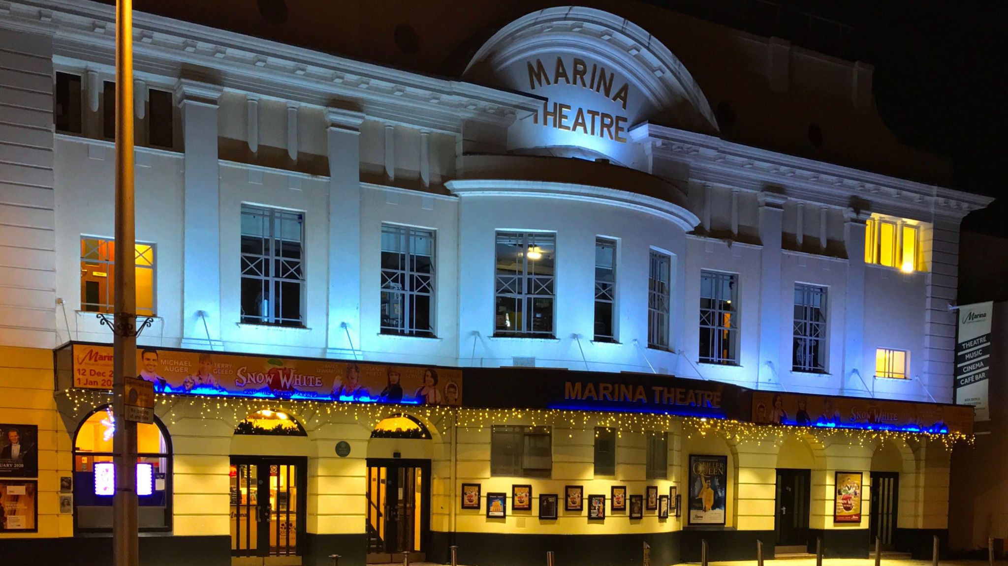 Facade of Marina Theatre lit up at night with light blue and yellow tones