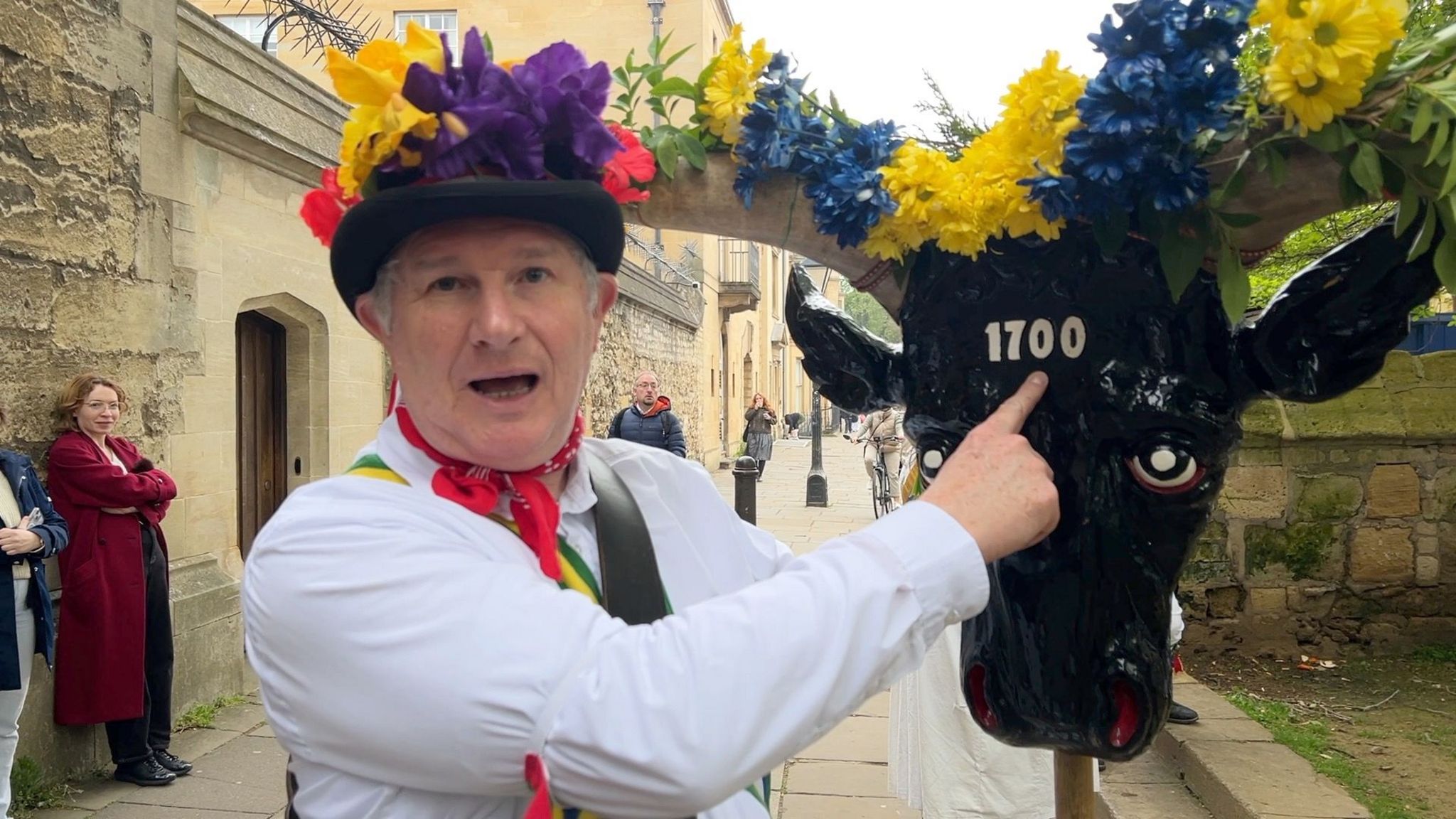 A morris dancer pointing towards a mask of a bul decorated with flowers
