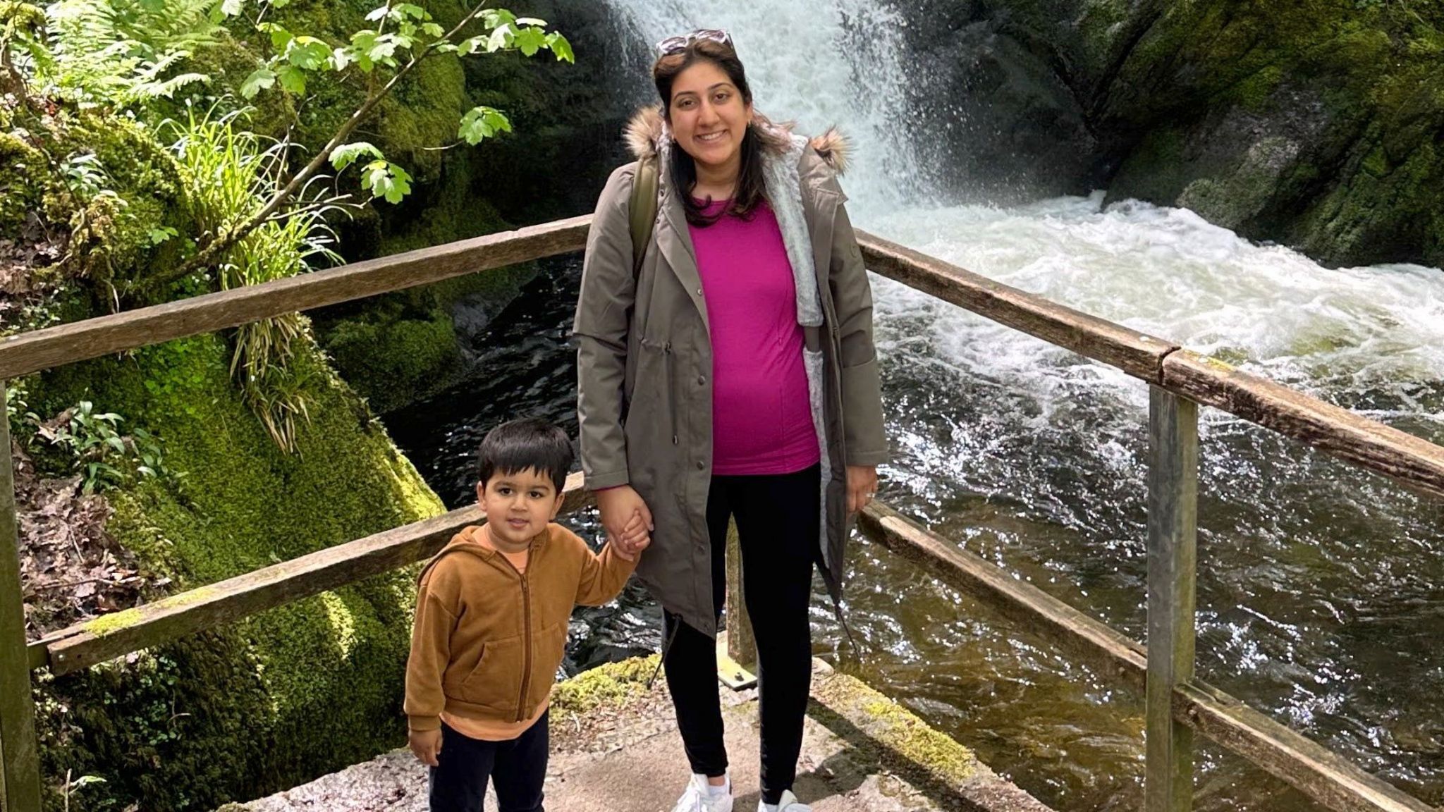 A mum holding hands with her toddler next to a waterfall