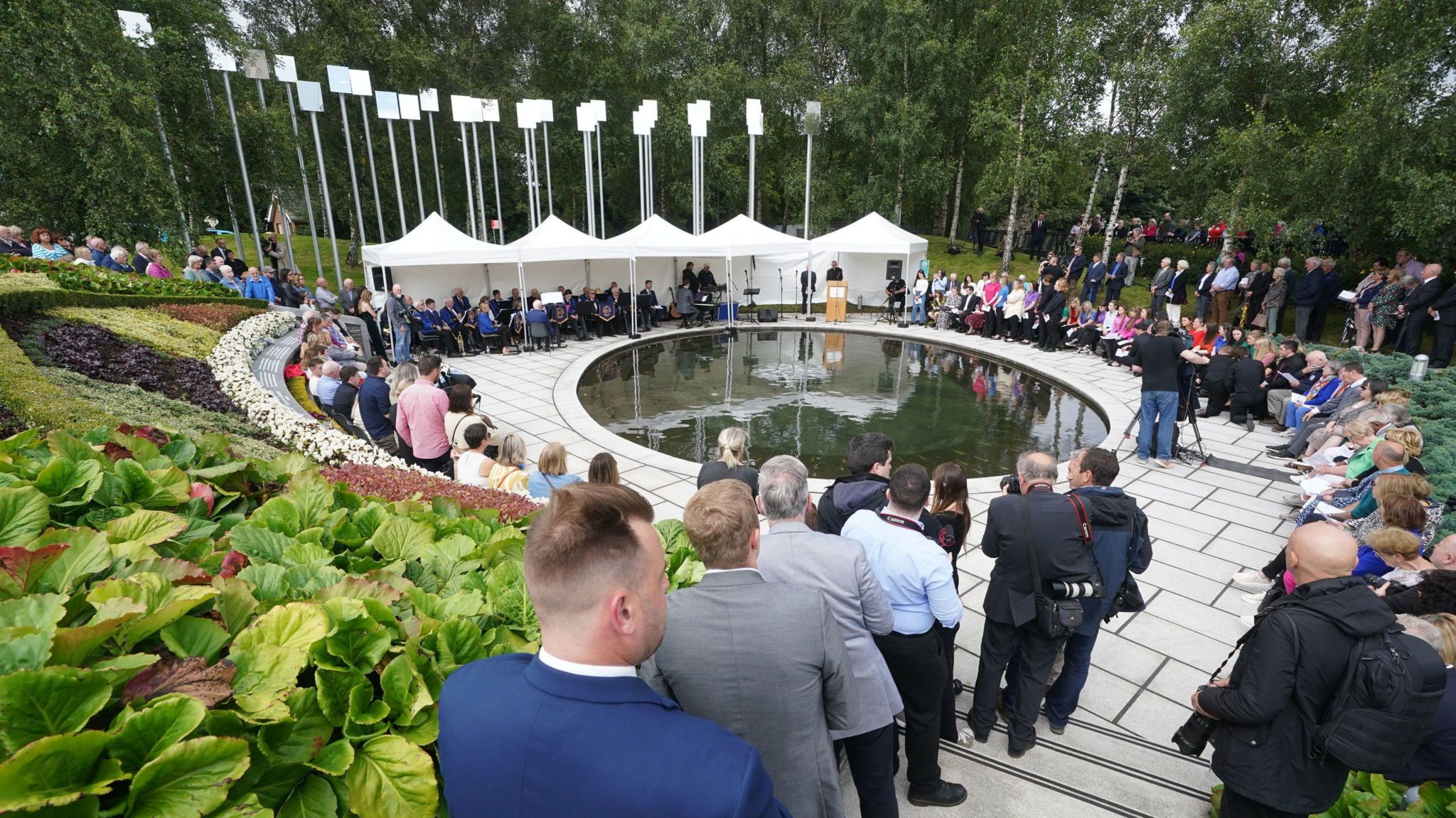 A group of people gather in the memorial gardens in Omagh, which features a small pond and 29 pillars to represent the victims, for the 25th anniversary of the attack