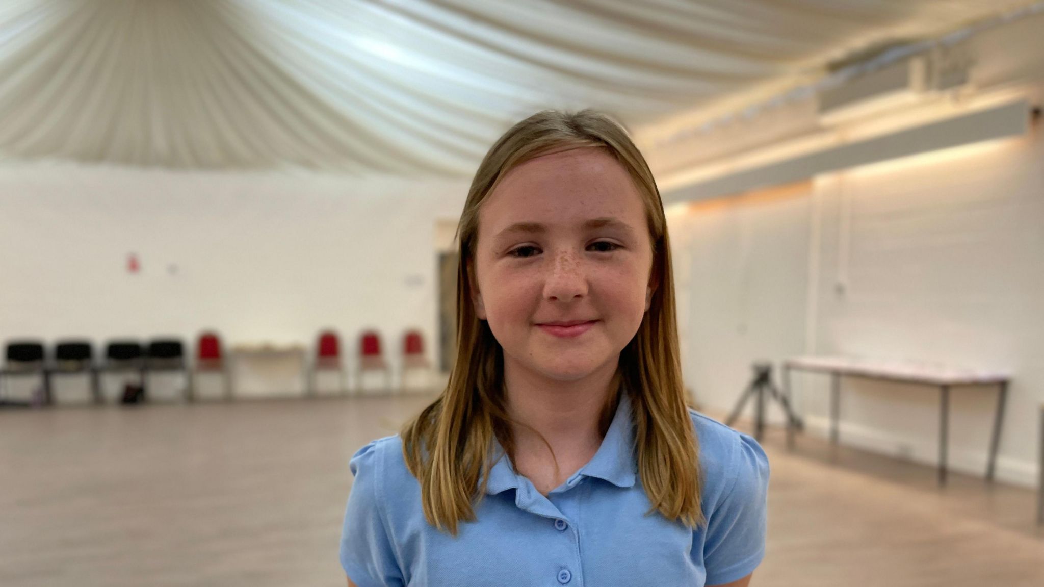 Grace in a blue polo shirt standing in a hall