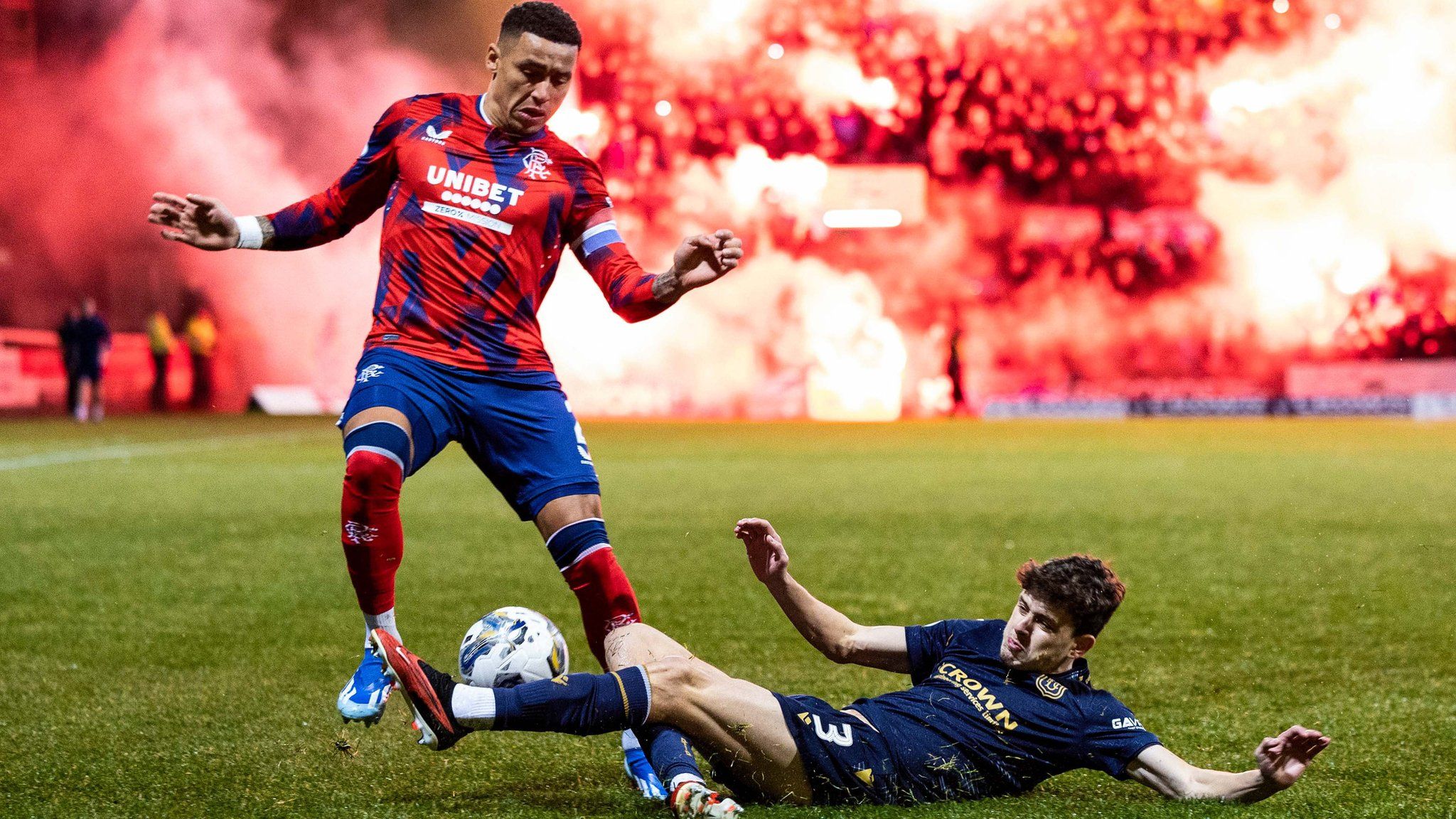 Rangers captain James Tavernier and Dundee player Owen Beck on the pitch as pyrotechnics go off in the background