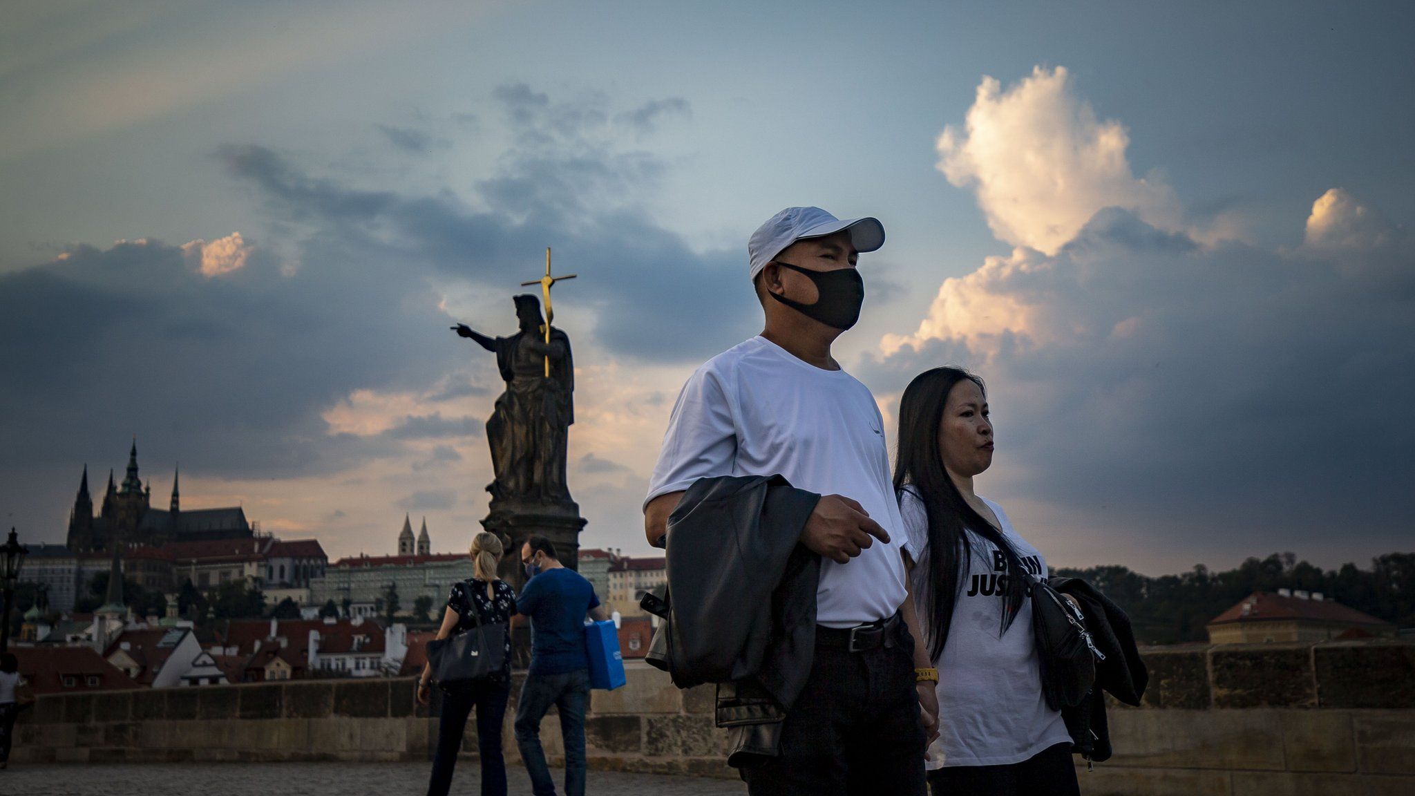 Tourists wearing face masks walk at sunset on medieval Charles Bridge on September 16, 2020, in Prague, Czech Republic.