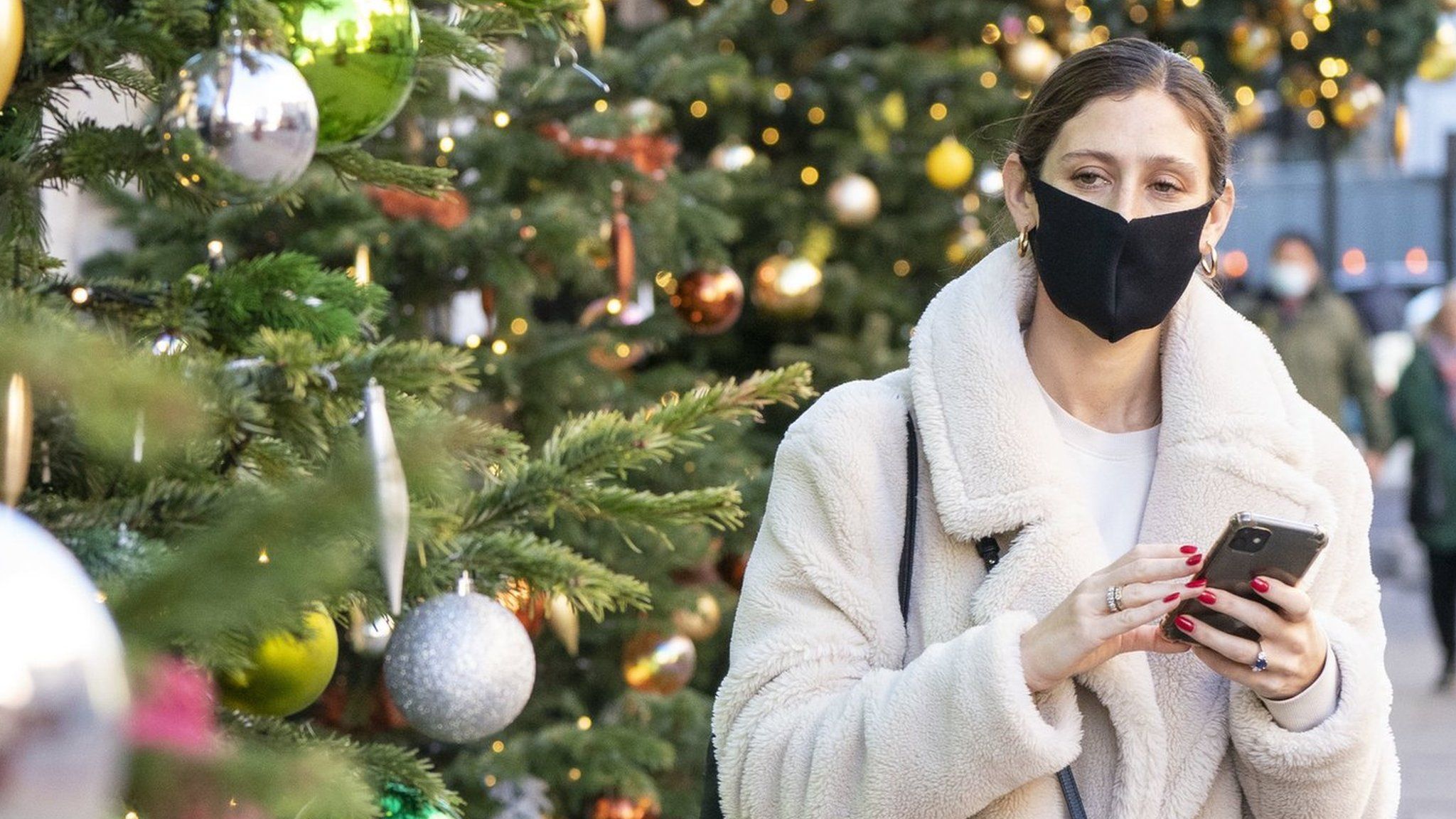 A woman wears a mask as she walks past Christmas decorations in London"s Knightbridge