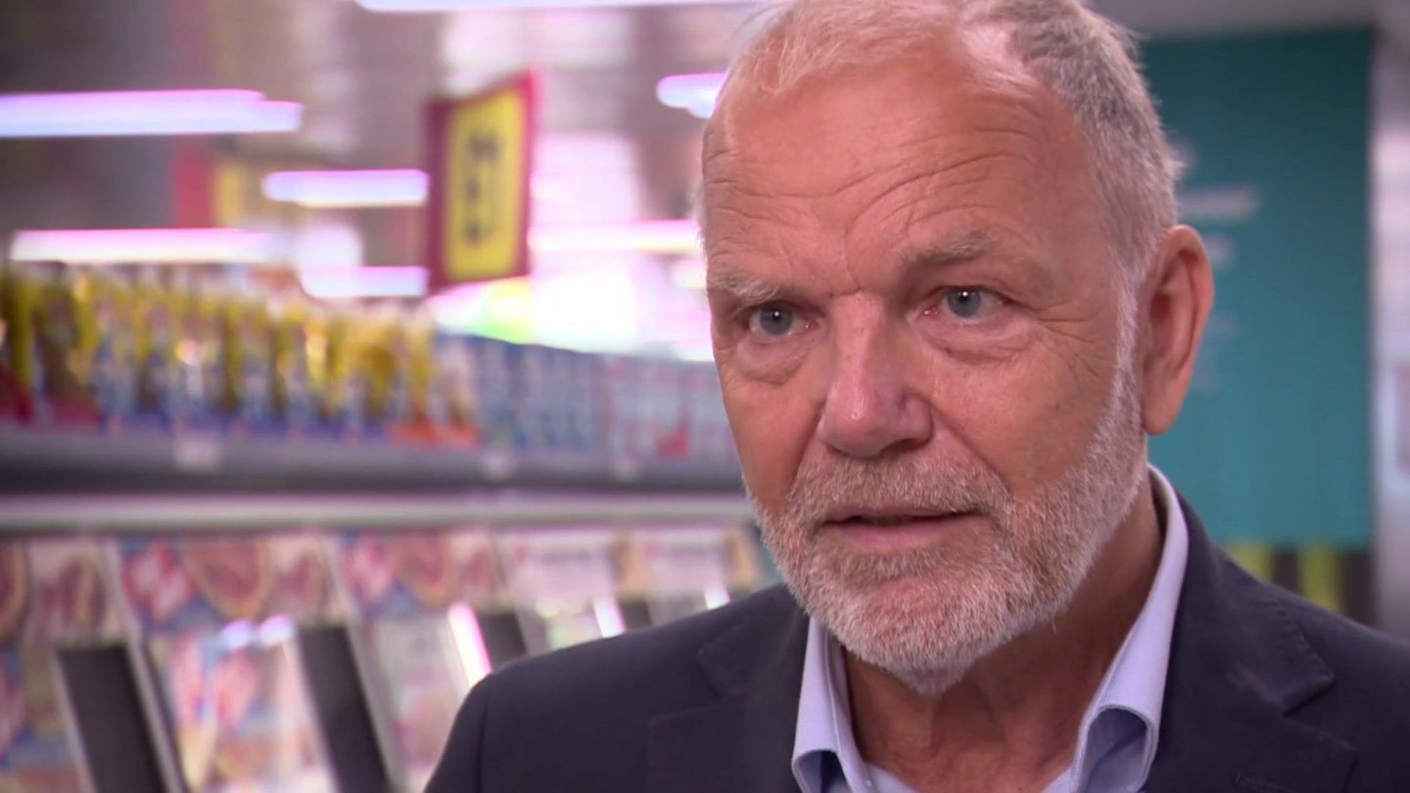 Paul Cowley, a man with grey hair wearing a suit, speaking to the BBC from a supermarket aisle