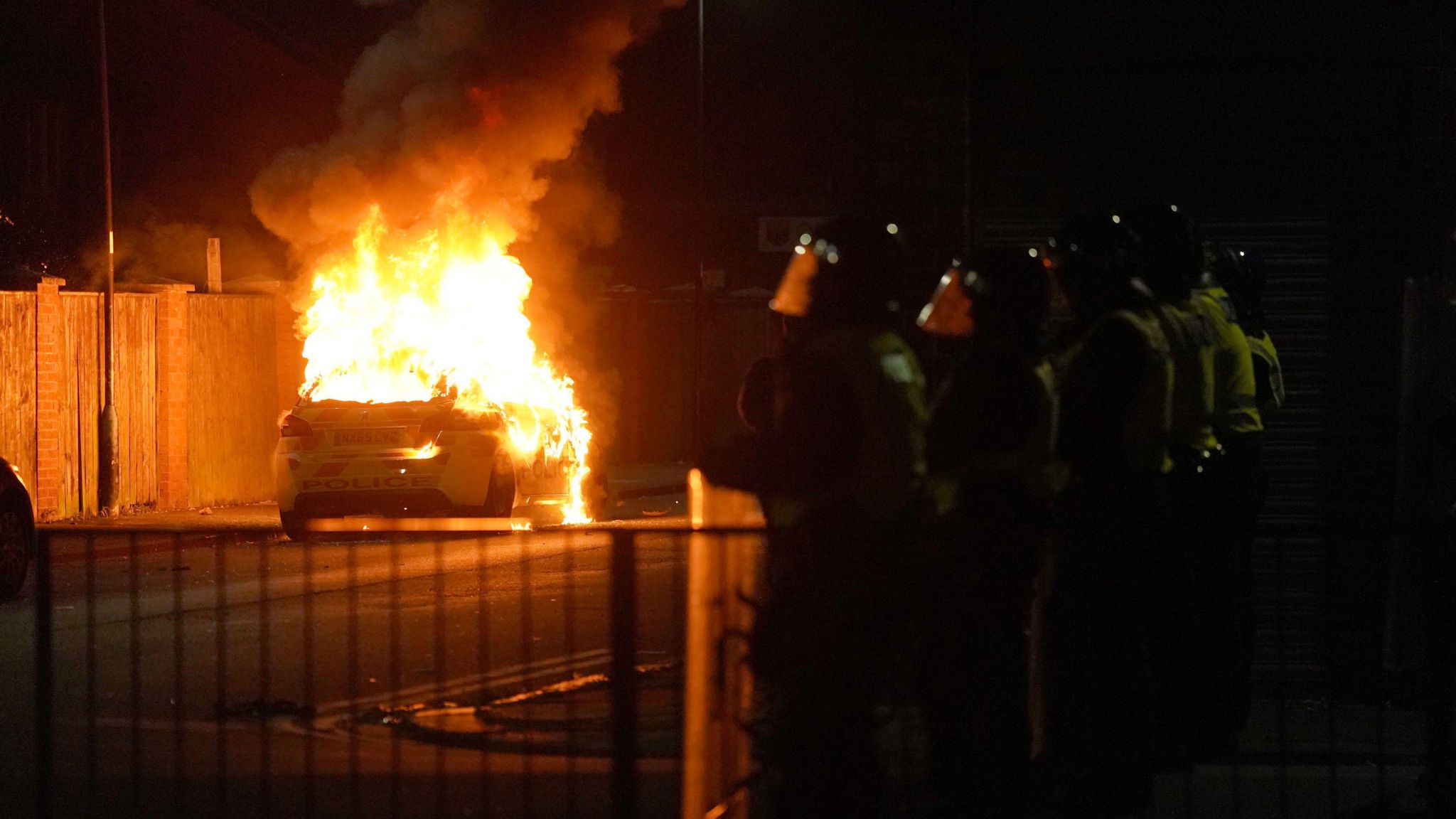 A car is on fire as police look on.