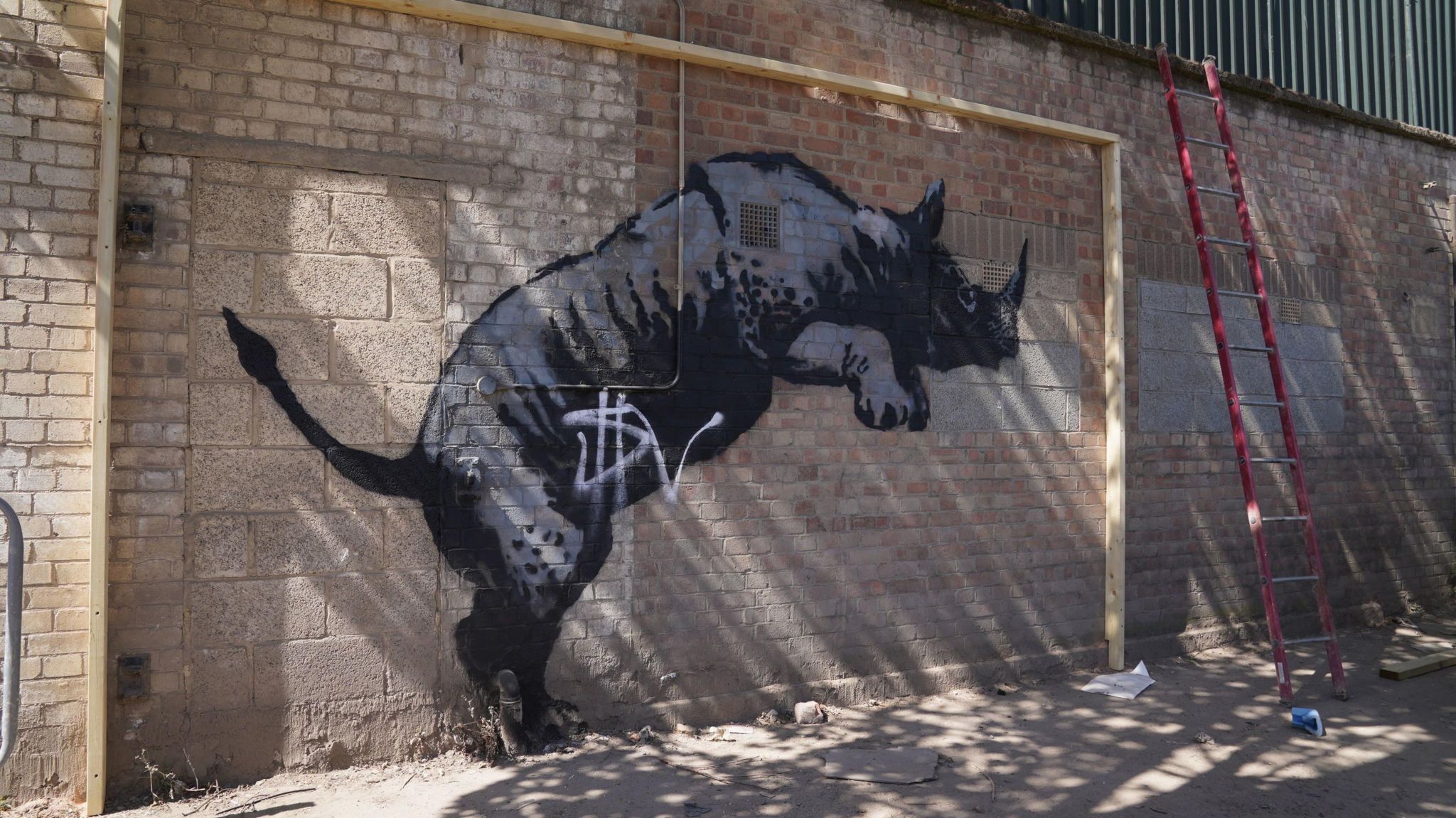 A black and grey painted rearing rhino on a light brick wall, with a white 'SV' tag sprayed over it