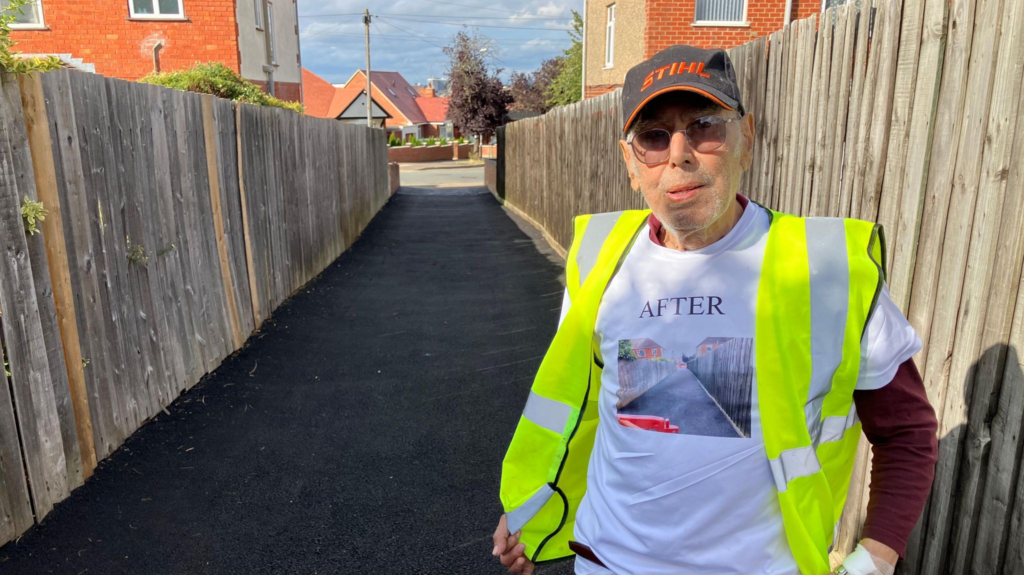 Chris Antoniou in a high-visibility jacket and white T-shirt stands proudly on a freshly tarmacked path