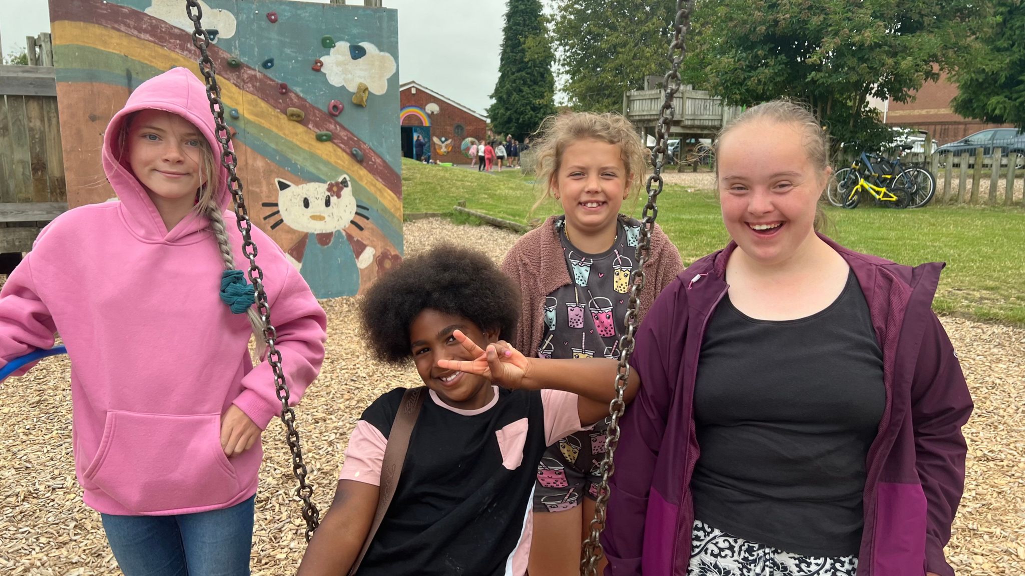 Four children in a playground outside smiling at the camera