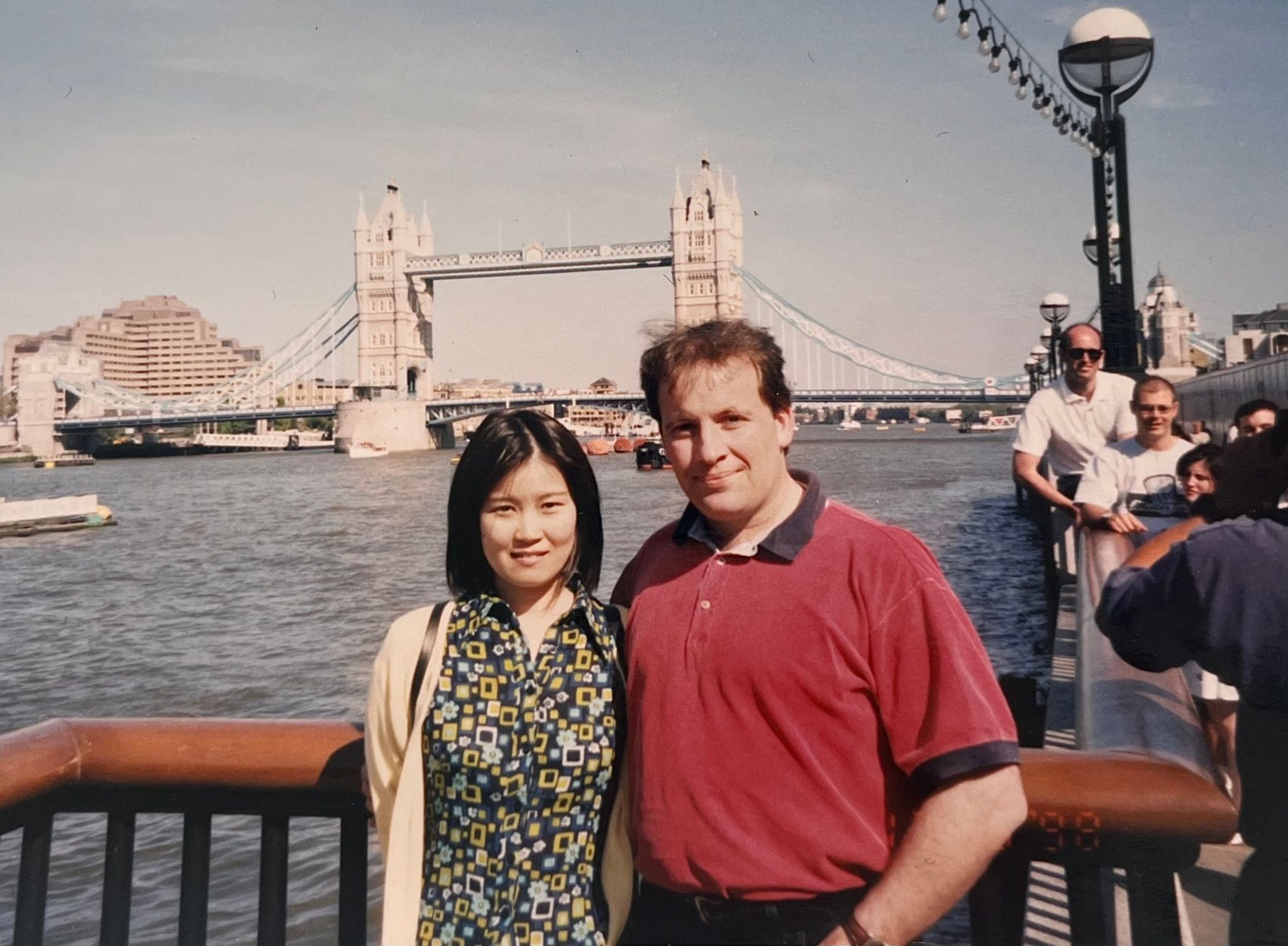 A Japanese woman and an English man stand for a photo in front of tower bridge in London