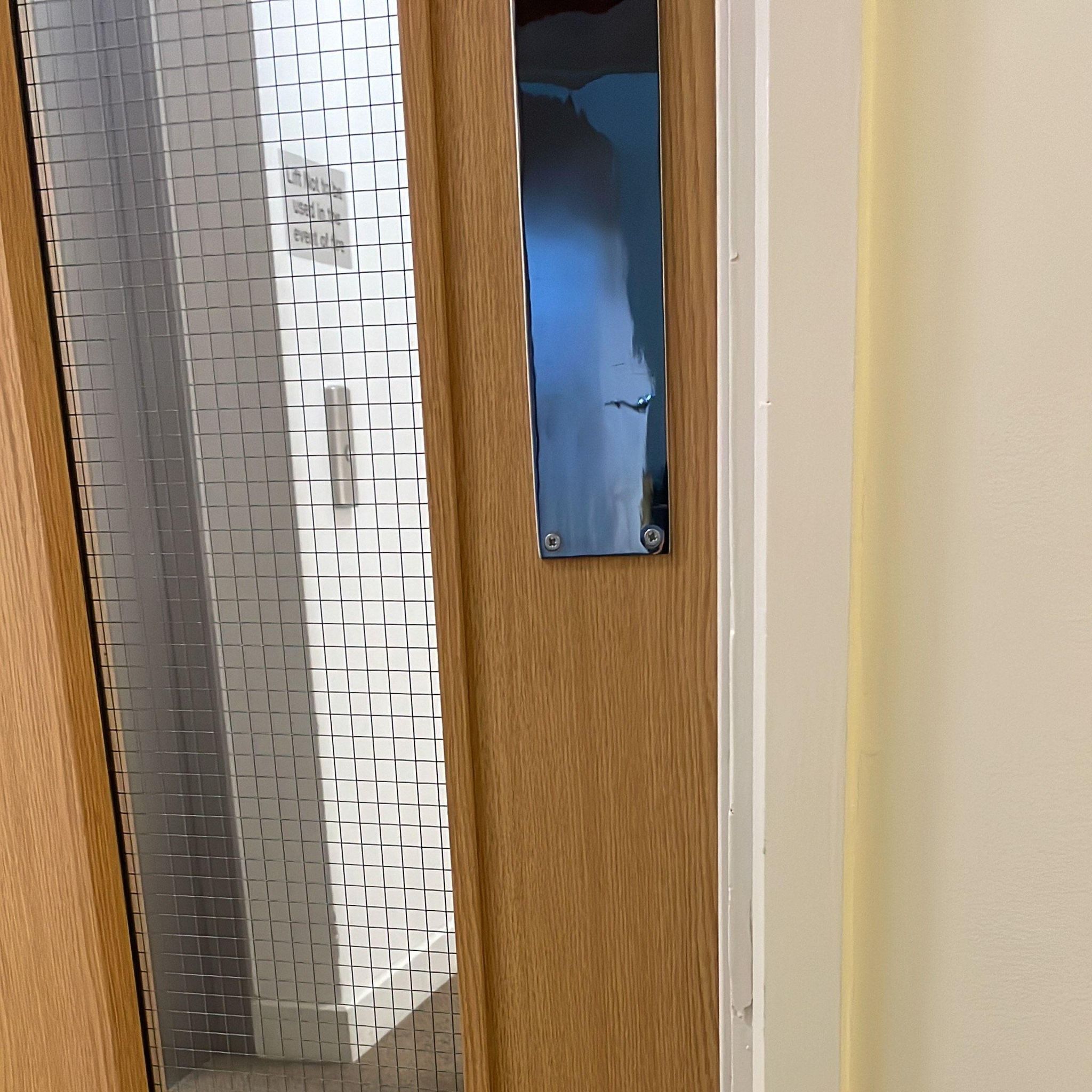 Image showing a view of a lift through a windoe in the locked wooden door in Abbi's building