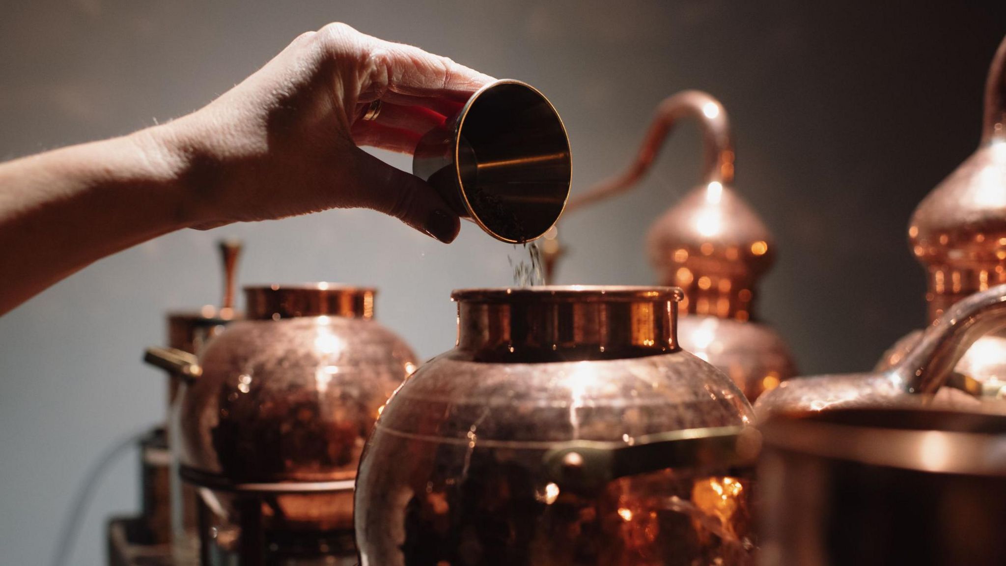 Hand pouring liquid into copper still - stock photo