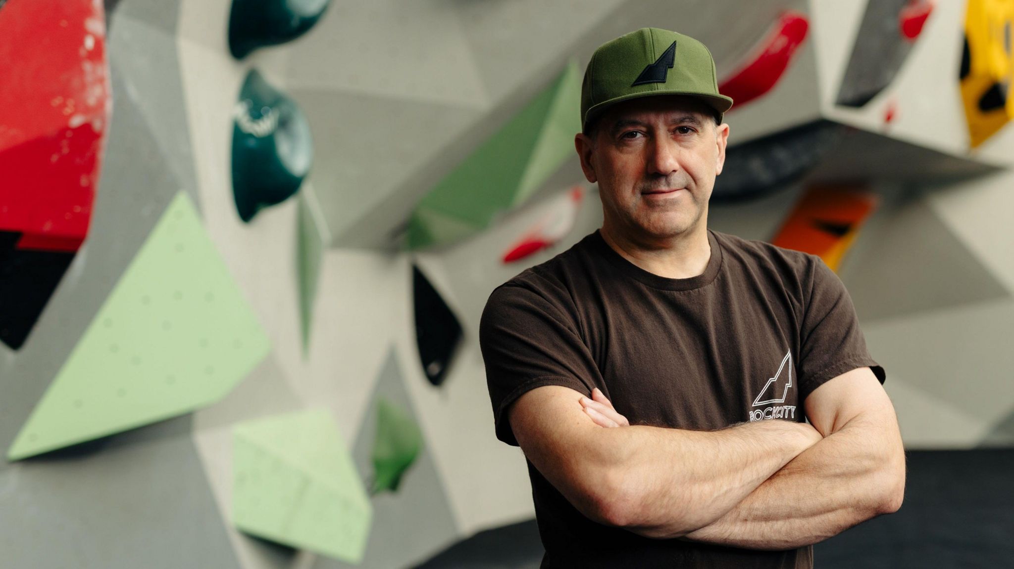 Managing director Mark English took, arms folded and wearing a black company branded t-shirt and green baseball cap, with a climbing wall in the background