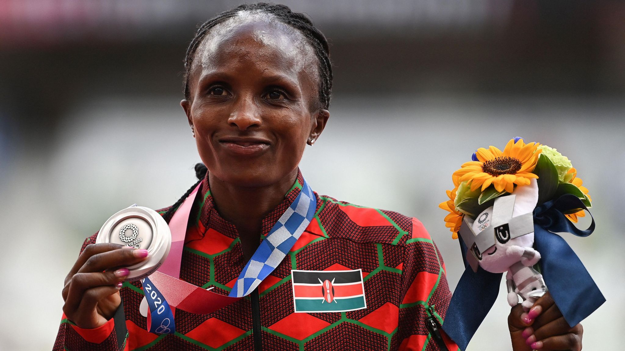 Hellen Obiri, wearing a Kenya tracksuit, poses with a silver medal and a bouquet of flowers at the Tokyo 2020 Olympics