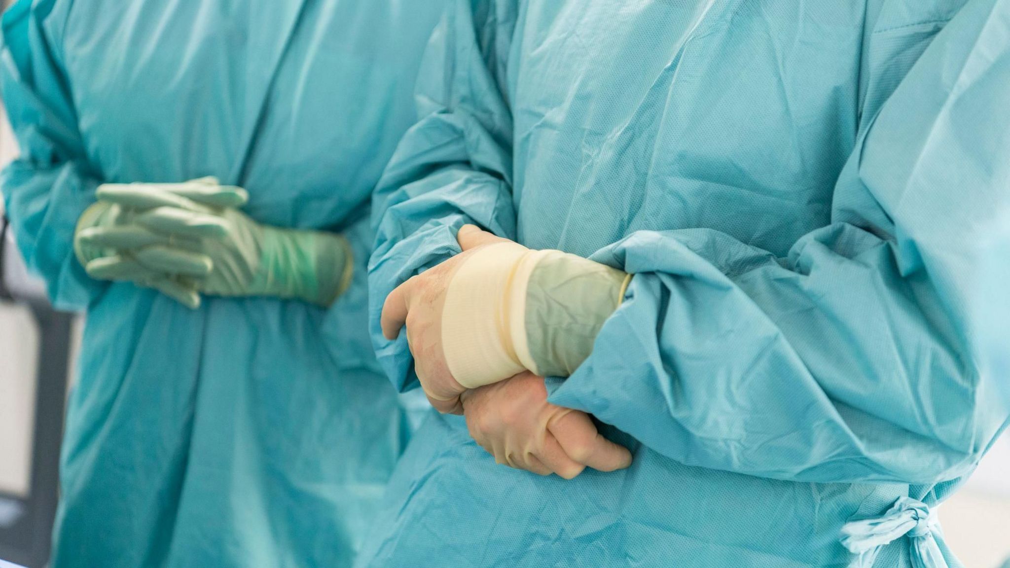 Two surgeons wearing scrubs and gloves, their arms crossed. We cannot see their faces. 