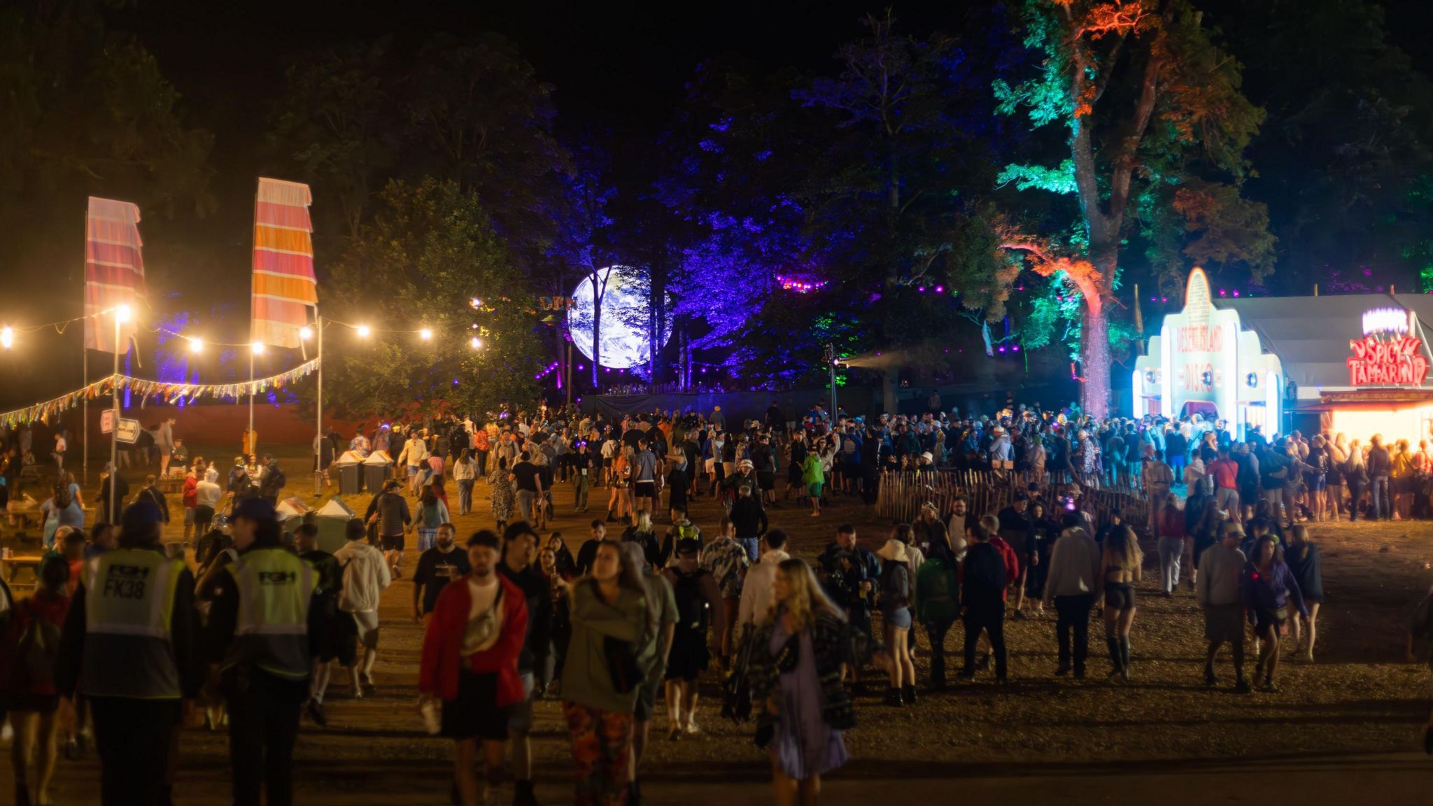 Crowds walking around the festival site with string lights, flags and an illuminated replica of the Earth in the background.