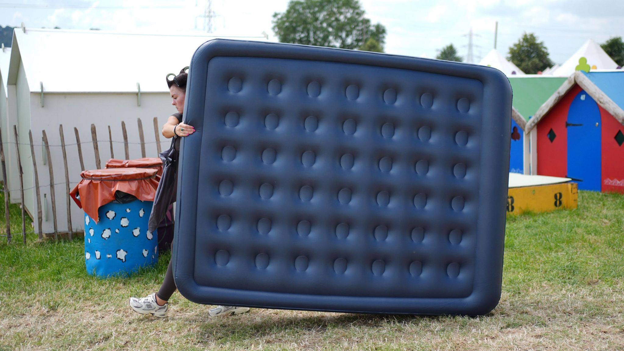 A woman carrying a blown-up blue air mattress across grass