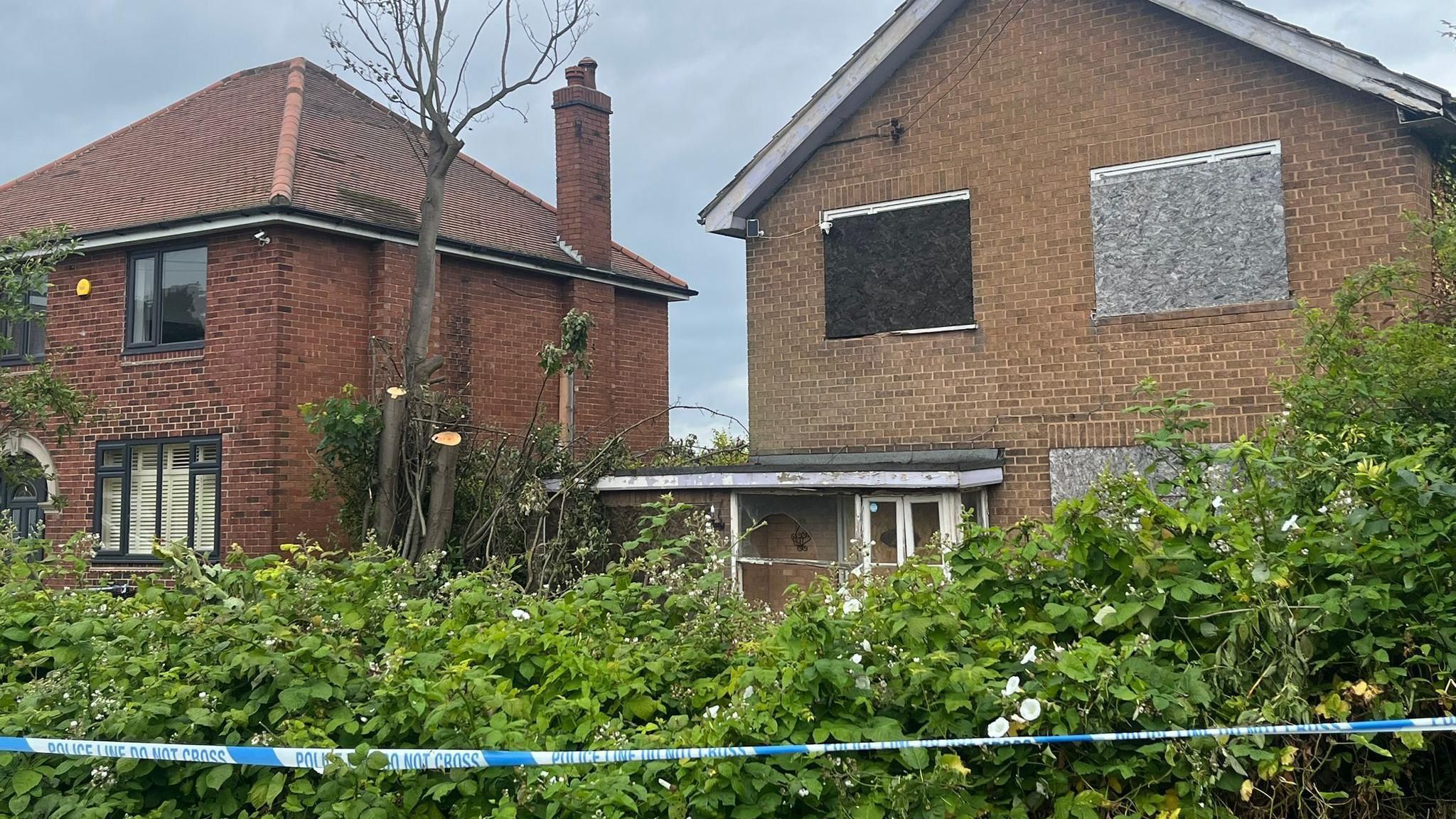 Police tape outside a boarded-up derelict house with a hedge in front of it in Carlton-in-Lindrick, Nottinghamshire