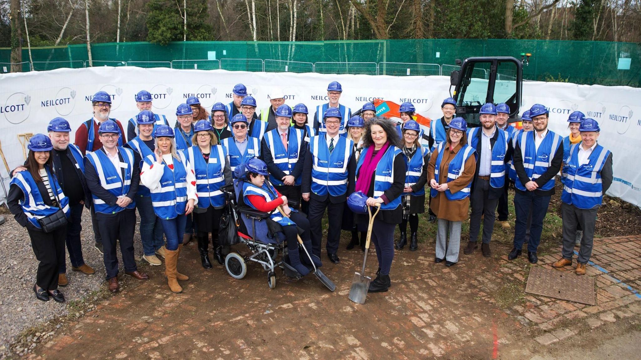 A group of people in blue high vis jackets and some with shovels smile for the camera