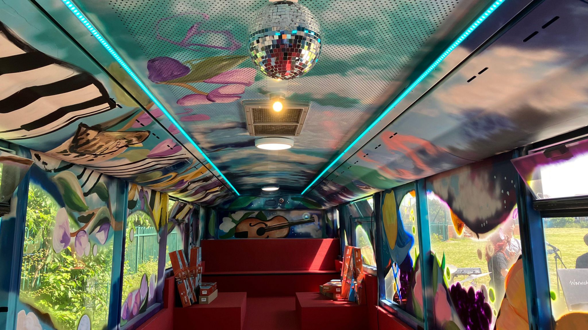 The inside of a bus that has been painted brightly, with sofas installed and a disco ball on the ceiling