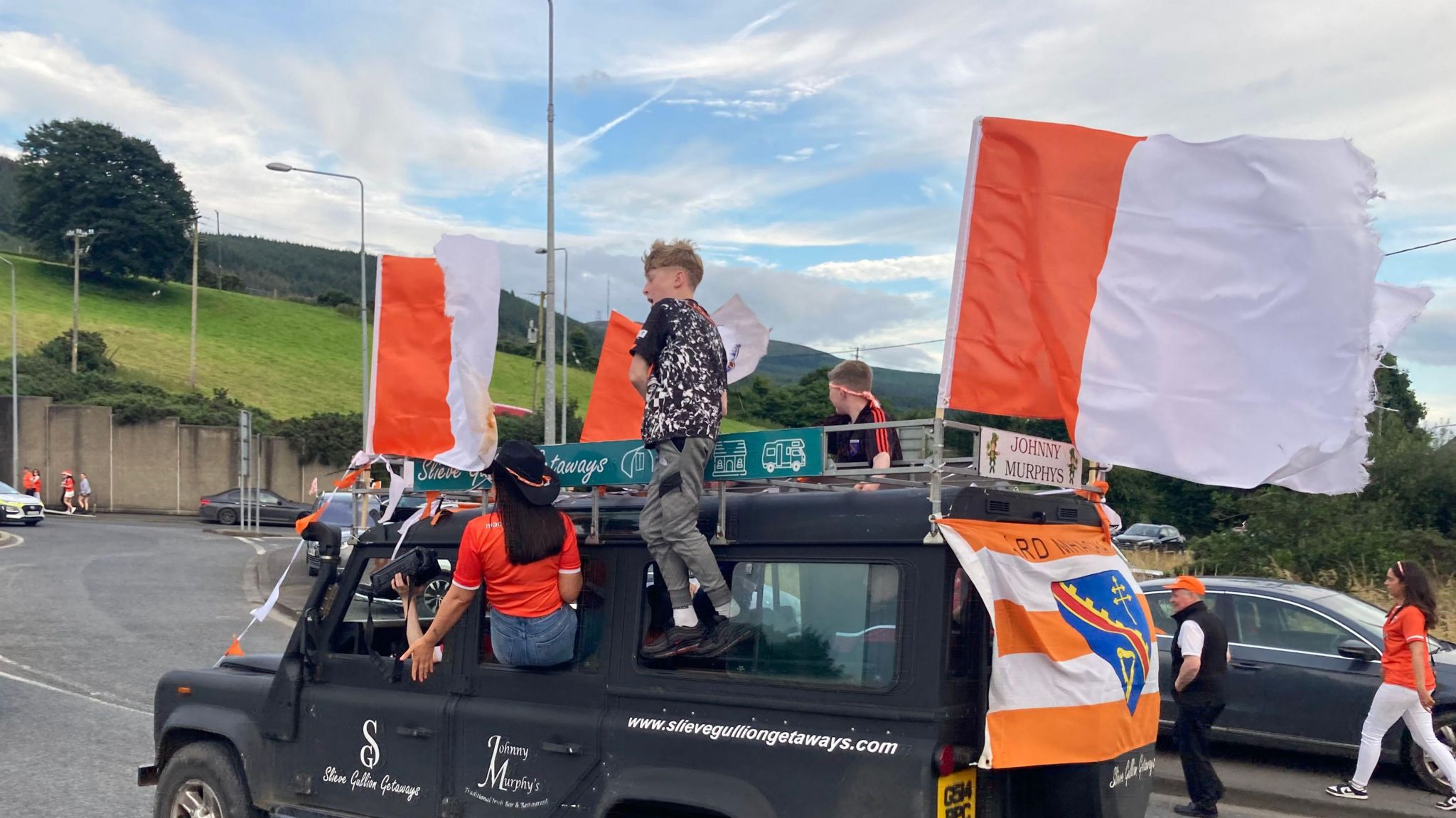 Armagh fans standing on a car that is decorated with the Armagh white and orange flags