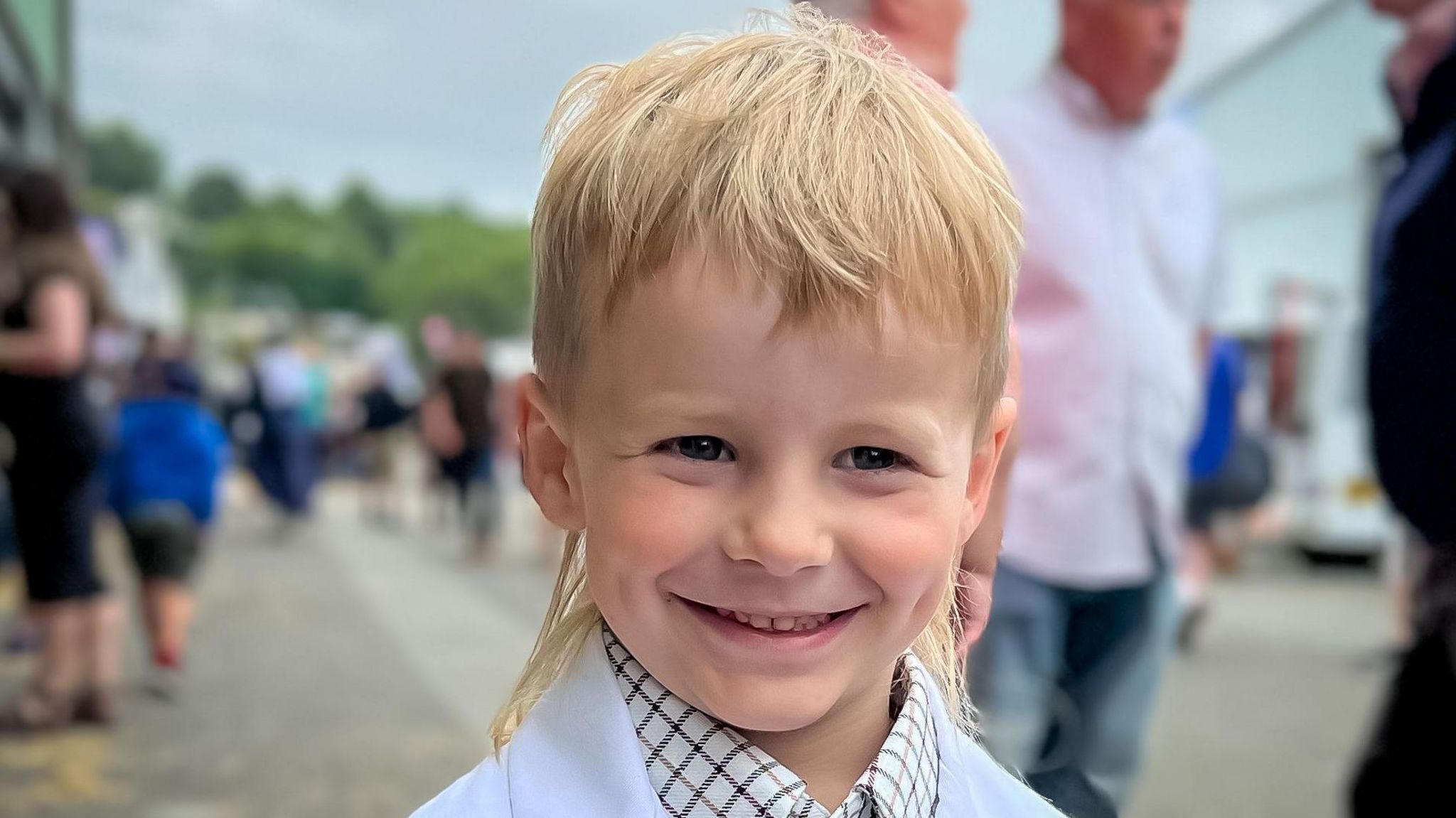 Boy in a sheep showing white jacket with a blonde mullet  