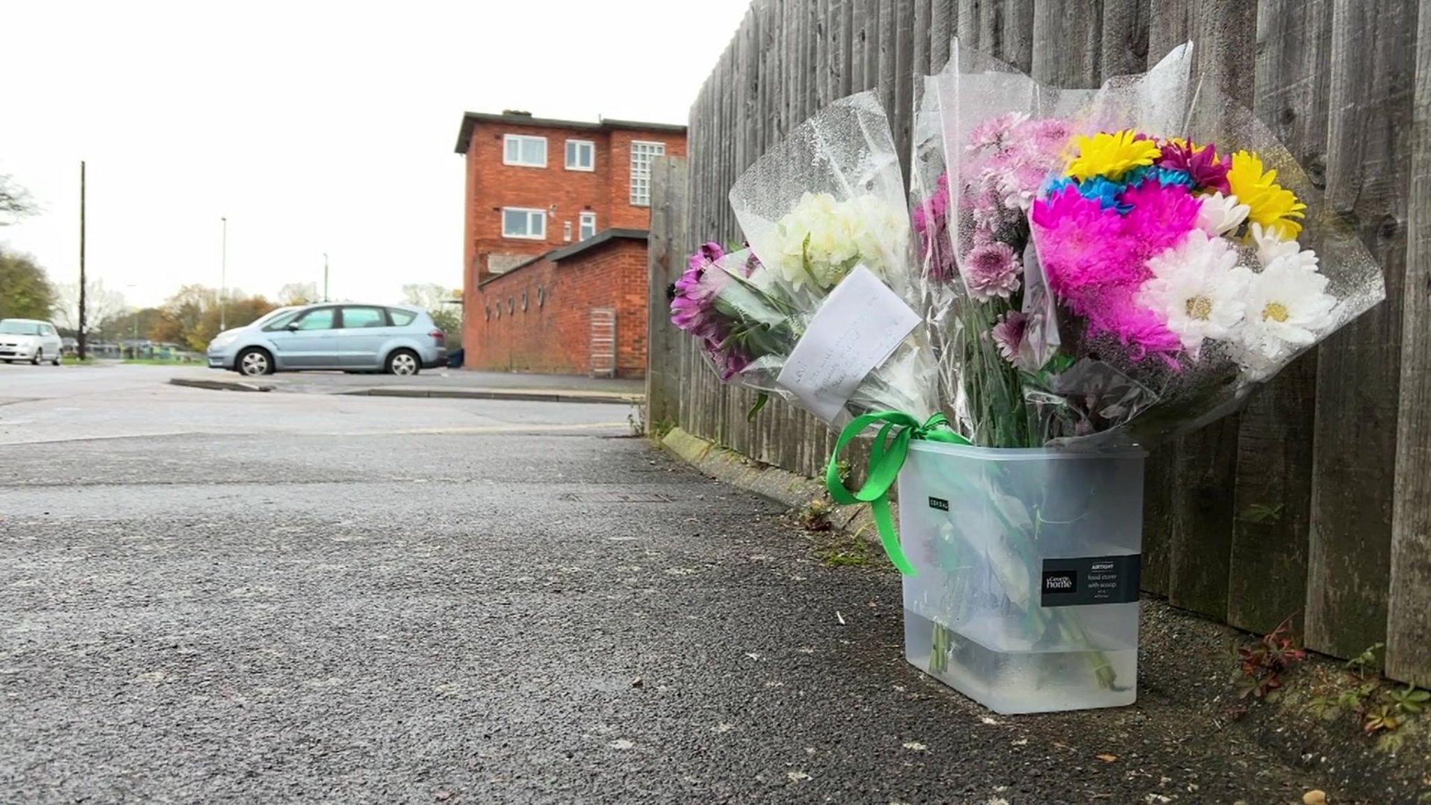 Bouquets of pink, yellow, blue and white flowers in a plastic tub filled with water and left against a fence in Keyes Road, at the spot where Levi Kent was fatally stabbed