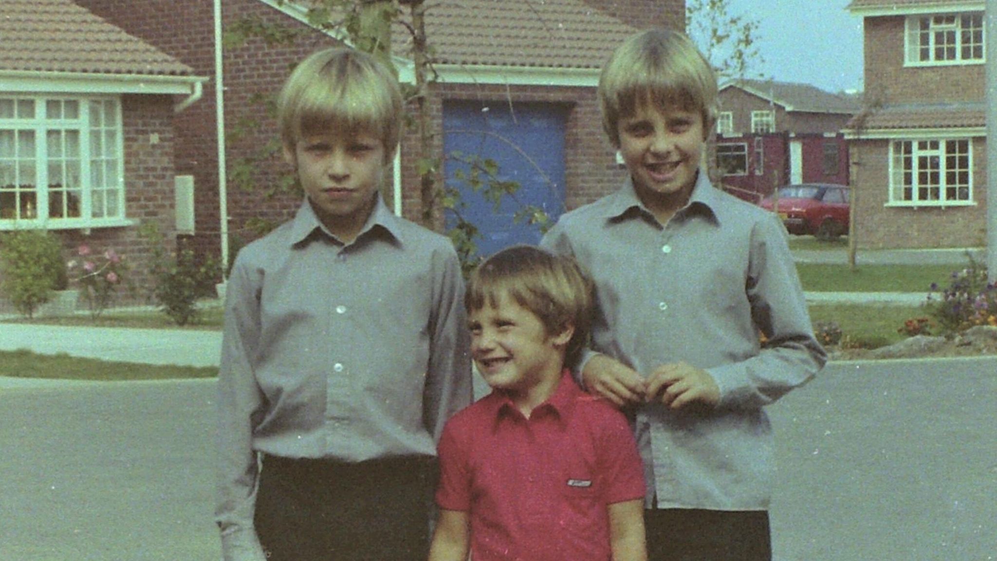 Steve Wyatt with his older twin brothers Rob and Mike smiling to camera. Circa 1980