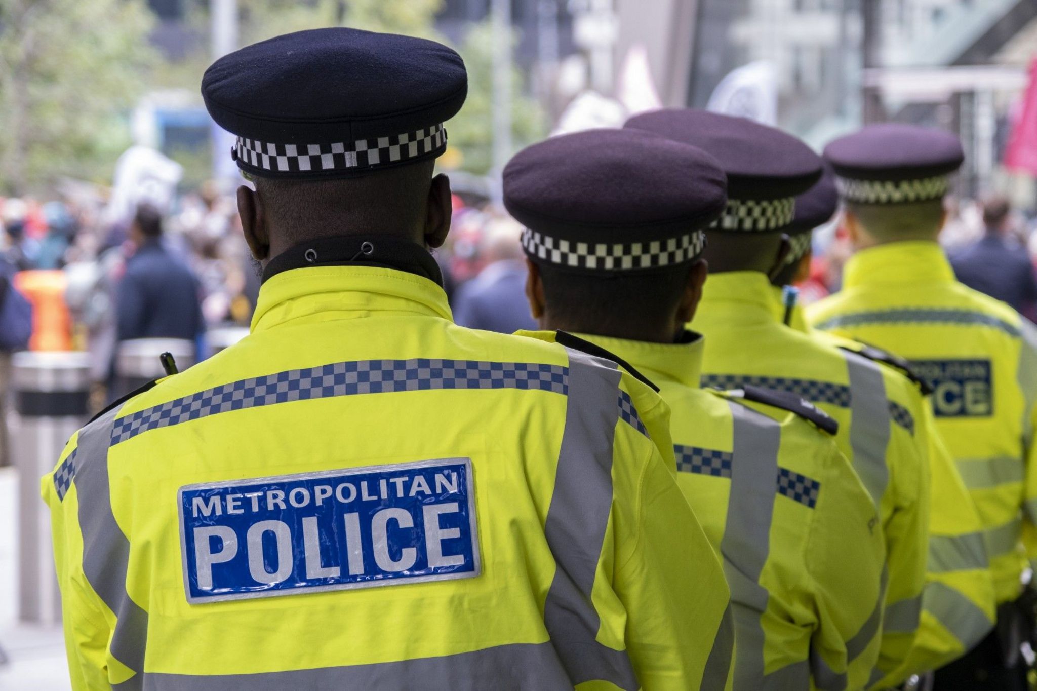 The backs of five Met Police officers, wearing hi-vis jackets with the name of the force on the back