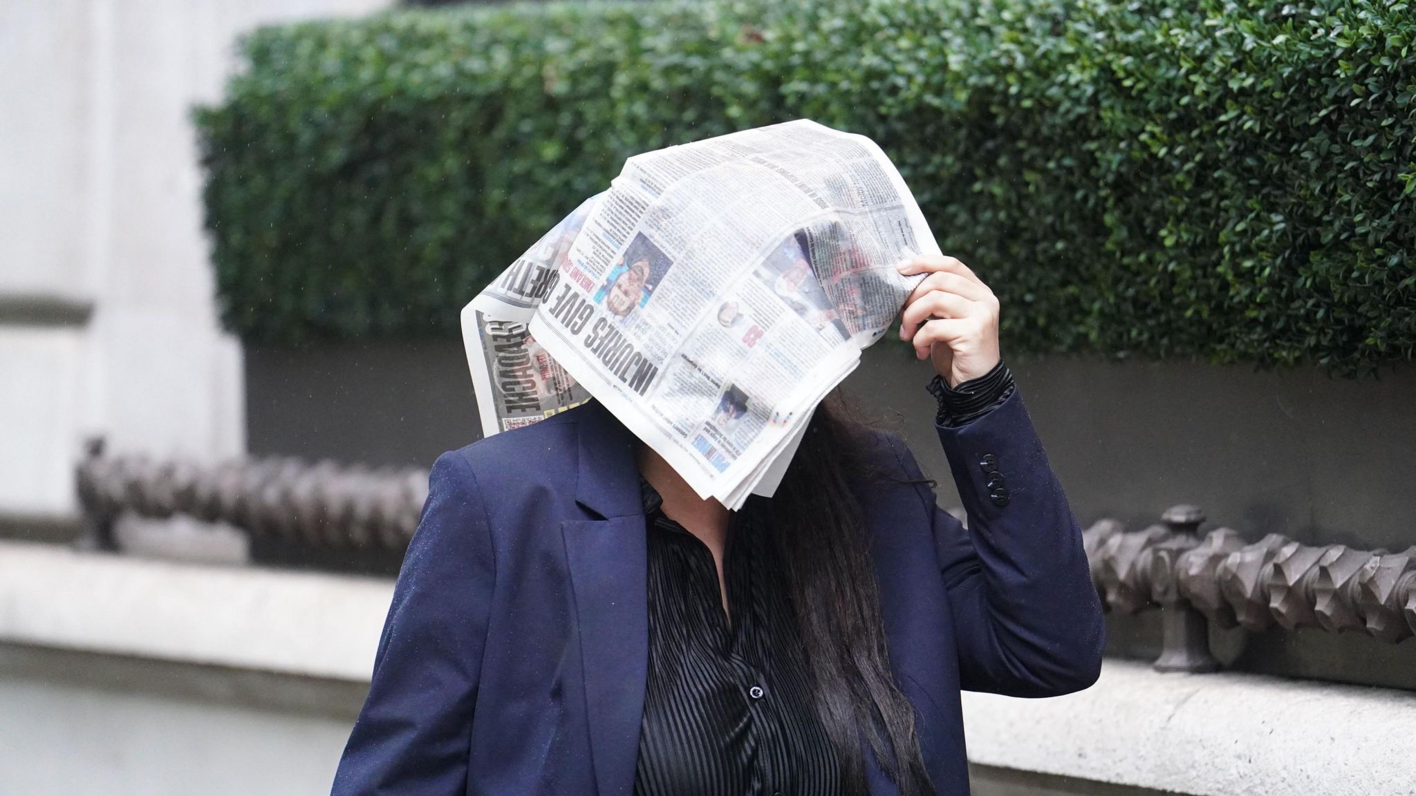 photo of a lady walking in the rain with a newspaper over her head
