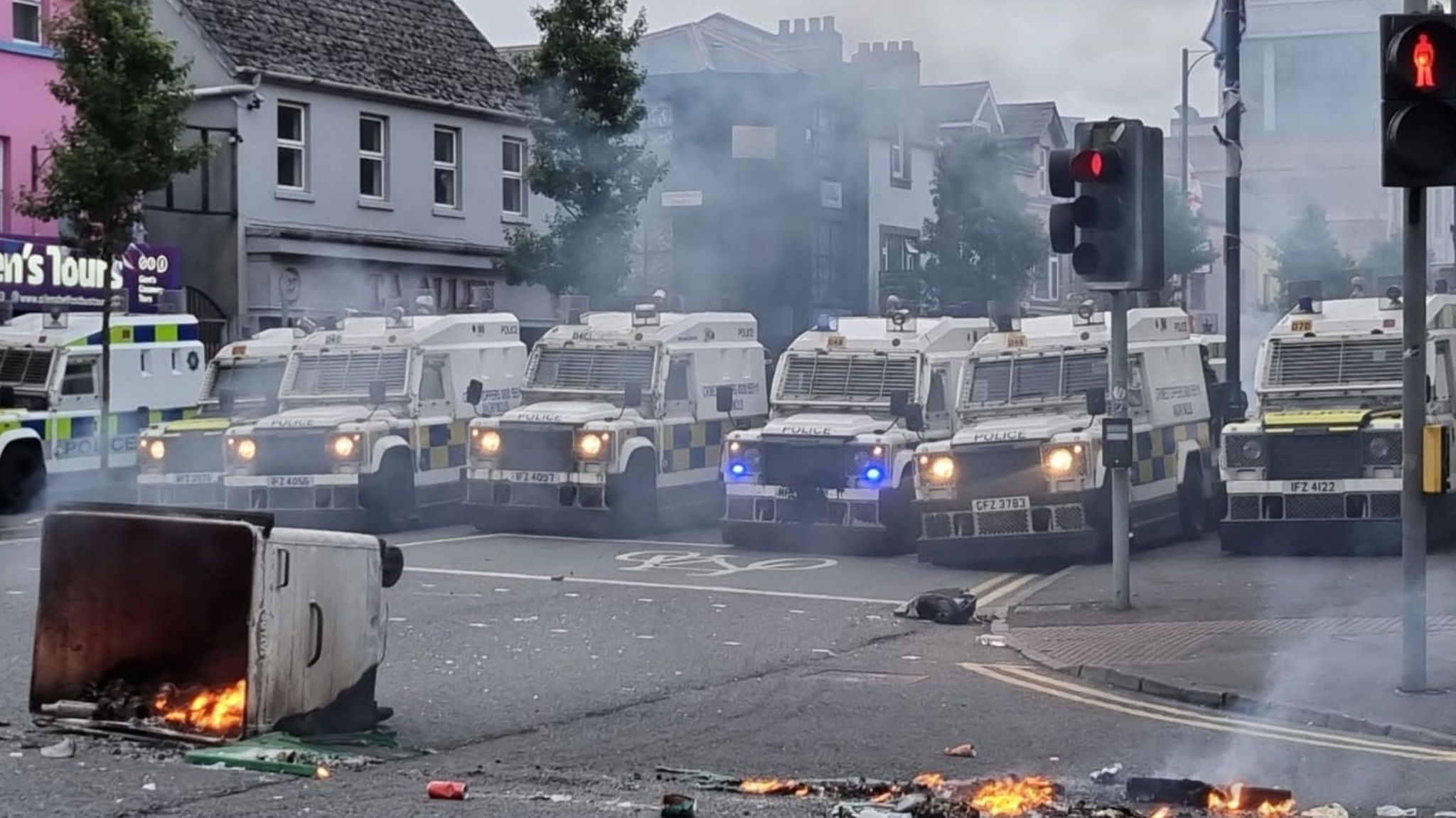 A row of PSNI Landrovers at a road block while a bin burns in front of it