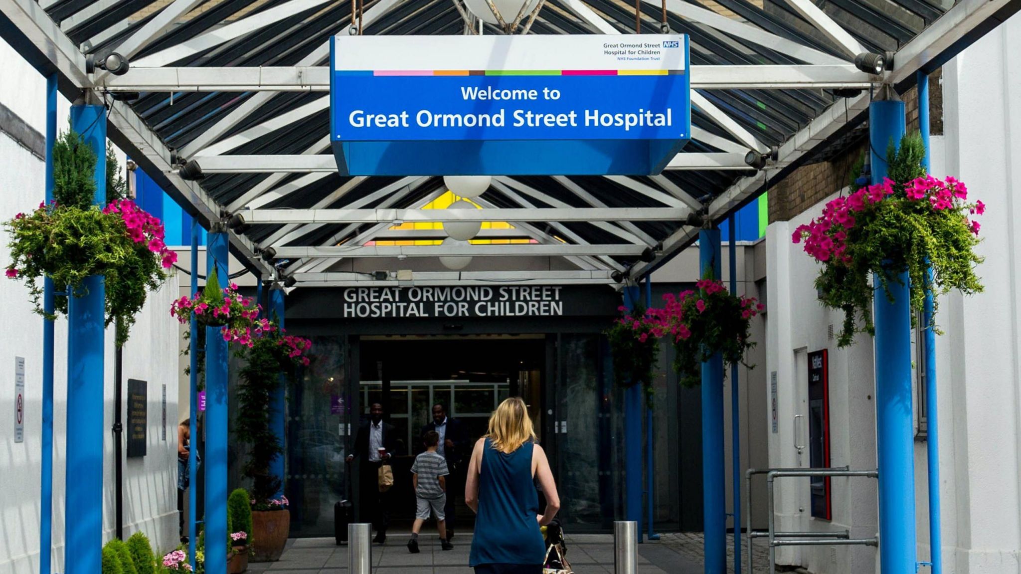 A woman walks under a sign for Great Ormond Street Hospital in its entrance. 