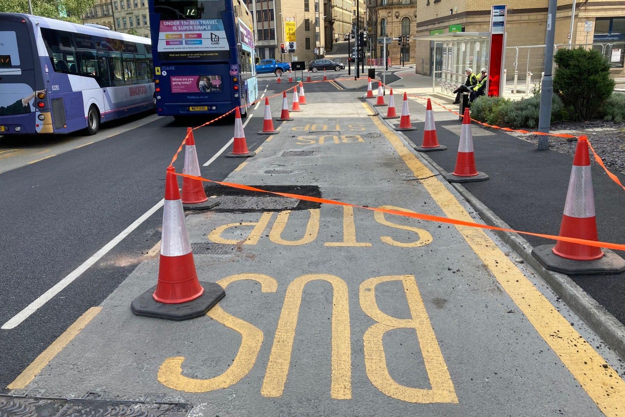 The damaged section of road with some recent repairs around a drain cover