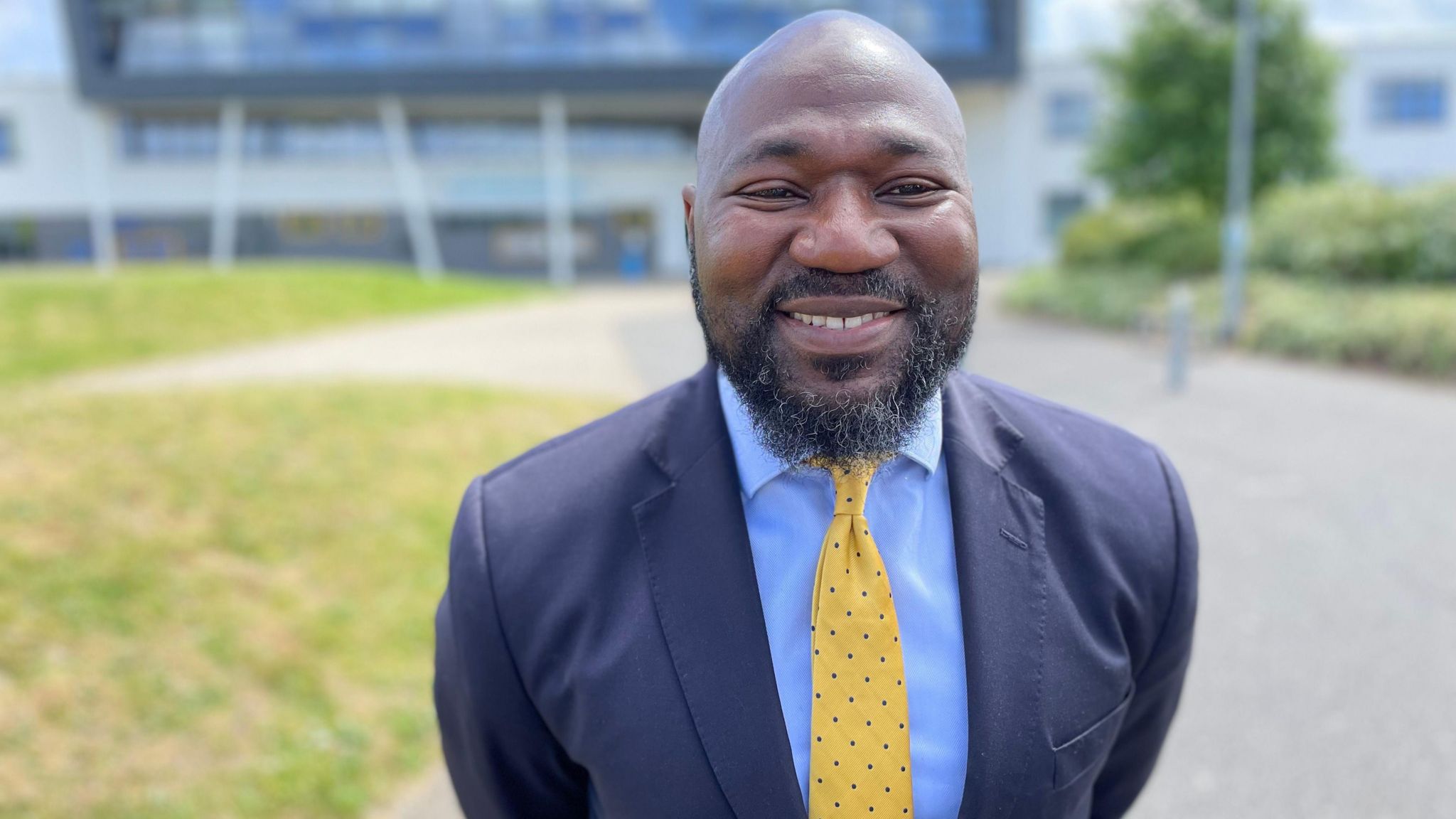 Festus Akinbusoye in a suit and yellow tie, smiling towards the camera