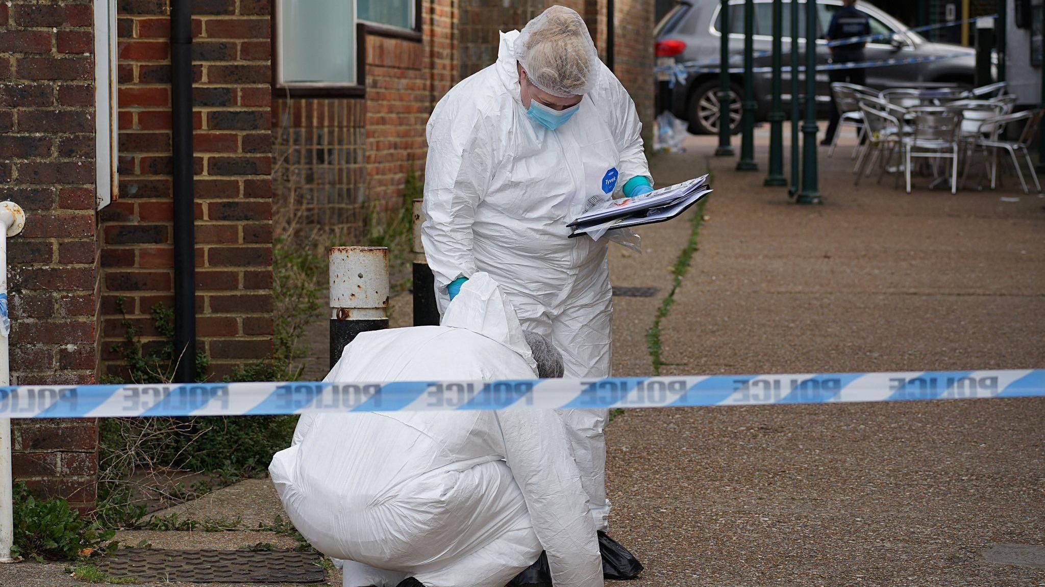 Two people in forensics clothing behind police tape