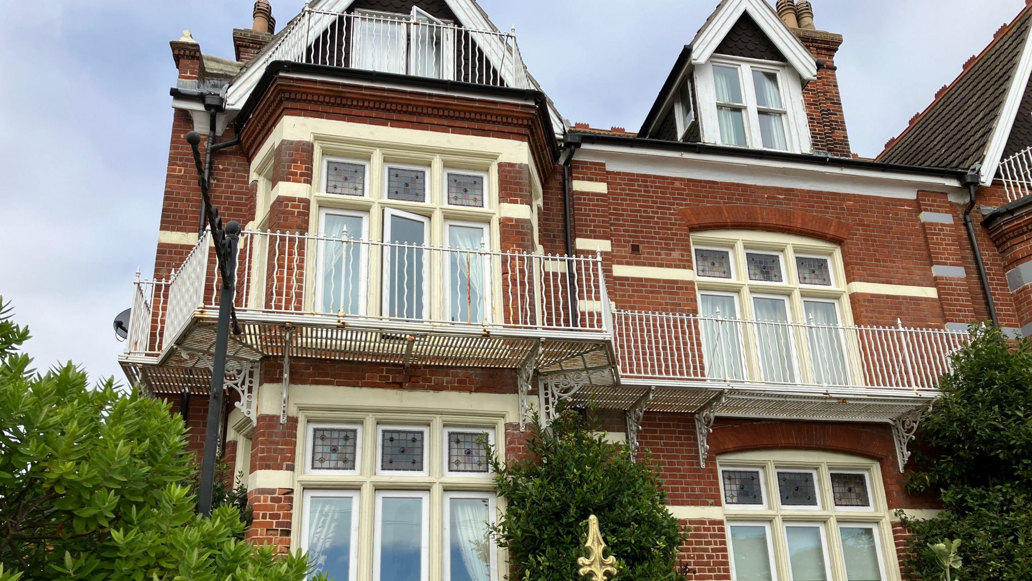 Red brick facade of the house with a white balcony and large white windows. 