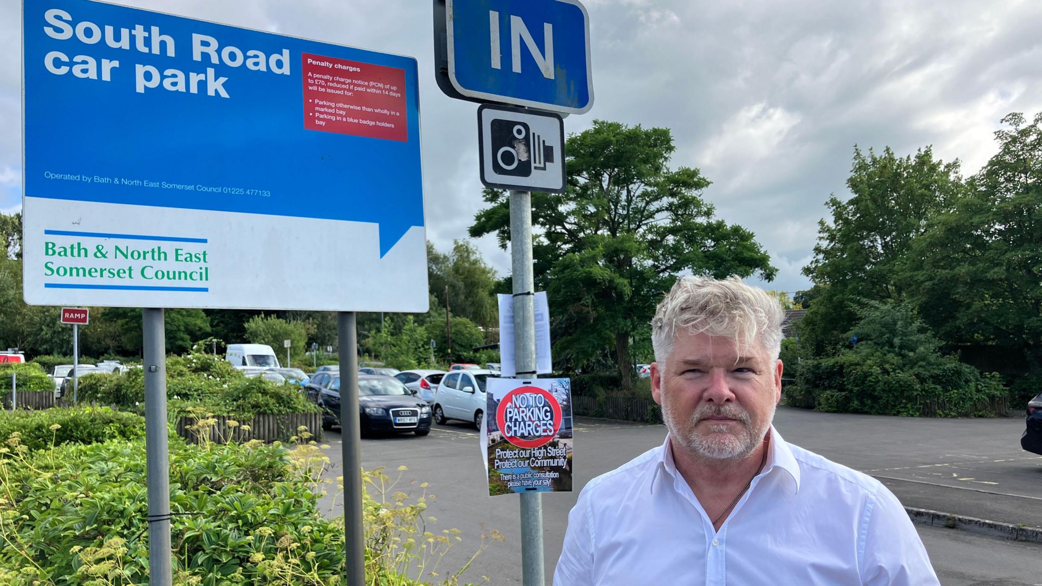 A blue signboard with white text saying South Road Car Park with a red box next to the text listing penalty charges. The bottom third of the signboard is white and has Bath and North East Somerset Council typed out in green text